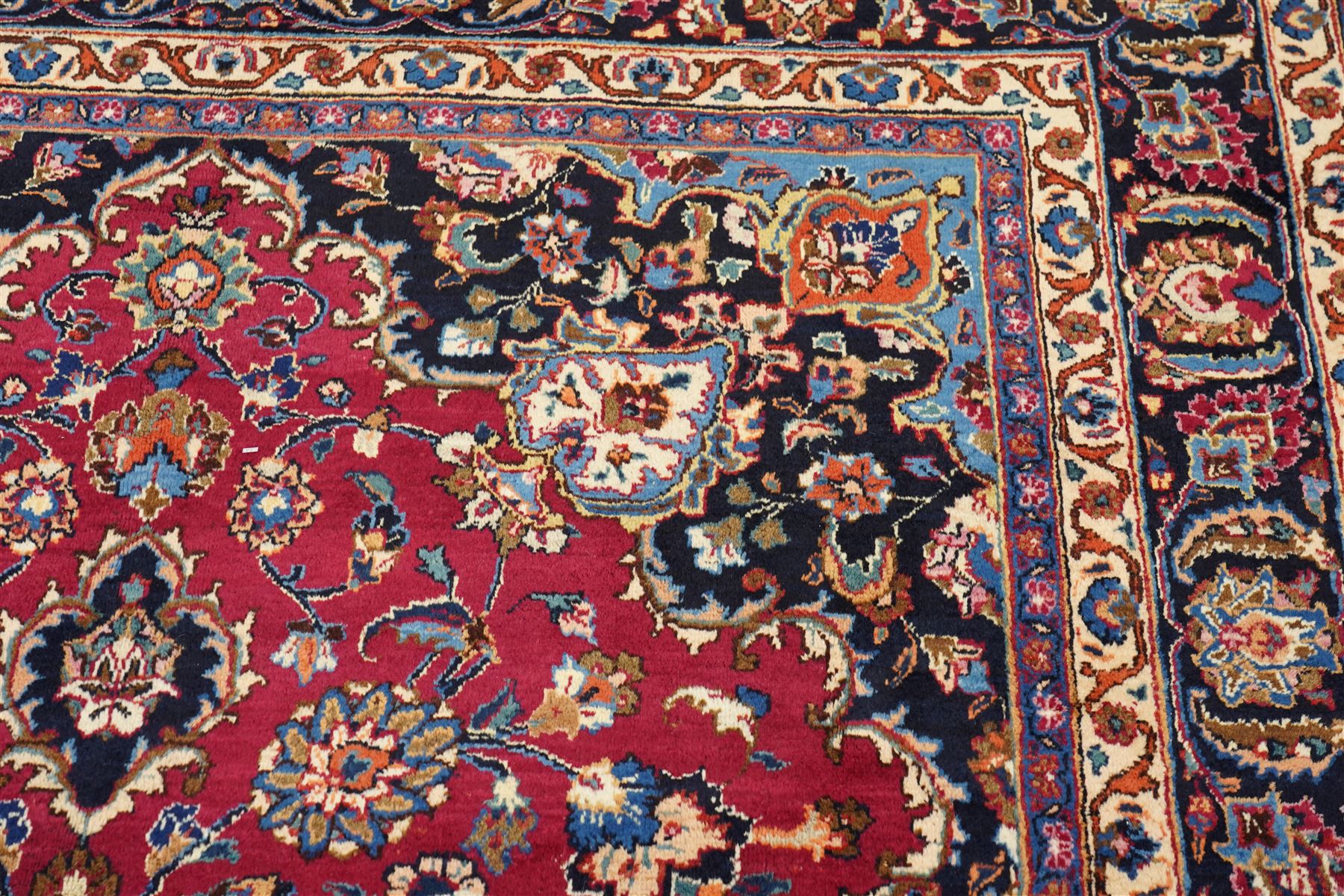 Central Persian Kashan hand-knotted carpet, rose red field, with central shaped lobed medallion issuing an all-over scrolling design of palmettes, floral sprays and arabesques, within conforming spandrels, enclosed by a broad indigo herati type palmette border framed by multiple guard stripes, in a palette of deep red, midnight blue and ivory tones, with cotton fringe ends, and Kashan signature 