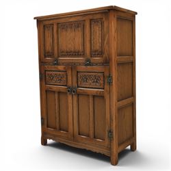 Old Charm - carved oak bar with three bar stools and associated Old Charm drinks cabinet, carved top with channels for glassware beneath, bar surface above glazed panels, shelves for glassware to the back, associated Old Charm drinks cabinet with fall front linenfold carving, above twin doors with shelved interior