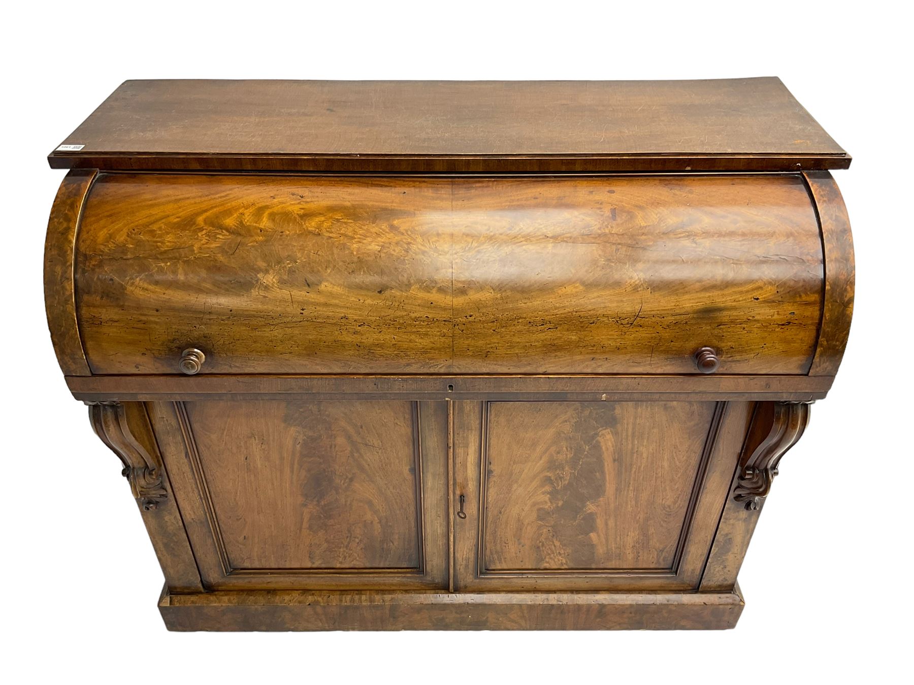 Victorian mahogany roll-top writing desk, top concealing fitted interior with pigeonholes and three drawers, the trisector inset writing surface with writing slope, base fitted with panelled cupboard enclosing single shelf, decorated with scrolled corbels