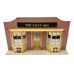 Scratch-built illuminated wooden doll's house type display of 'The Cock Inn' public house, the hinged front opening to reveal a single room furnished with bar, dresser, tables, chairs, stools, figures, bench seat, coat stand and various accessories L51cm H28cm D29.5cm