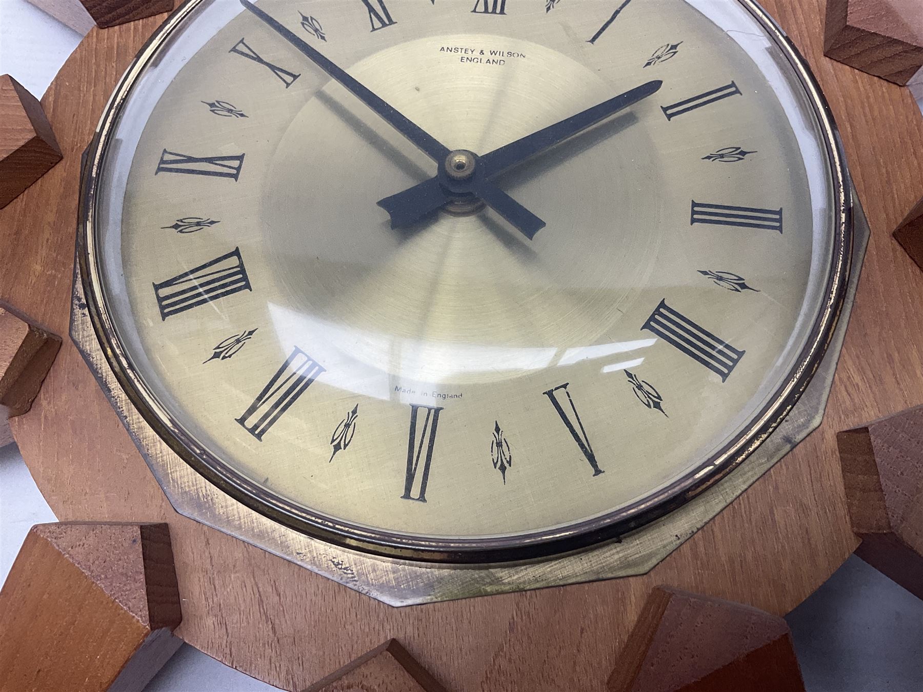 Mid-century teak sunburst wall clock by Anstey & Wilson, modelled with angular teak rays spreading from circular mount with plain brass face with Roman numerals, with battery operated Japanese movement, D45cm