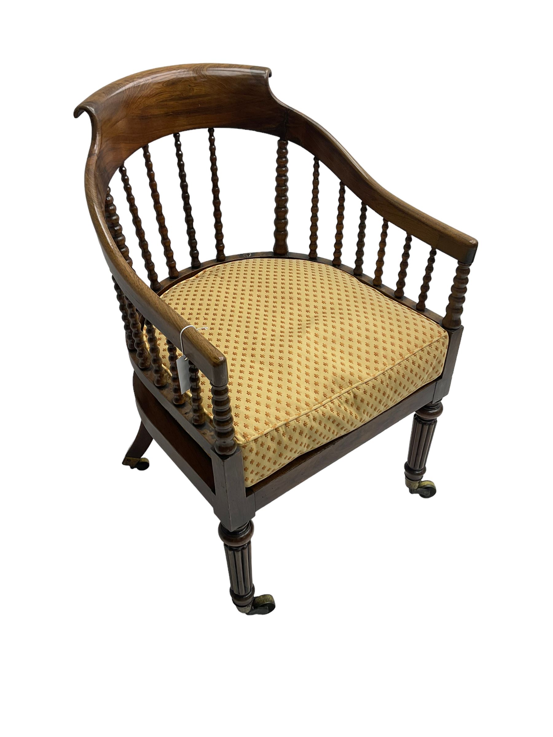 William IV rosewood tub armchair, the arched bow cresting rail over graduated bobbin turned spindles, cane seat with loose cushion, terminating in brass cups and castors.