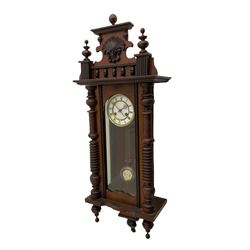 A  German spring driven wall clock c1900 within a glazed case with side panels and a full-length arched door and ornately carved pediment, turned finials and original pendant finials, with a 5' two-piece white enamel dial with roman numerals, minute markers and pierced steel gothic hands, with a visible gridiron pendulum with an R/A inscribed pressed brass bob, eight-day movement striking the hours and half hours on a coiled gong.  



