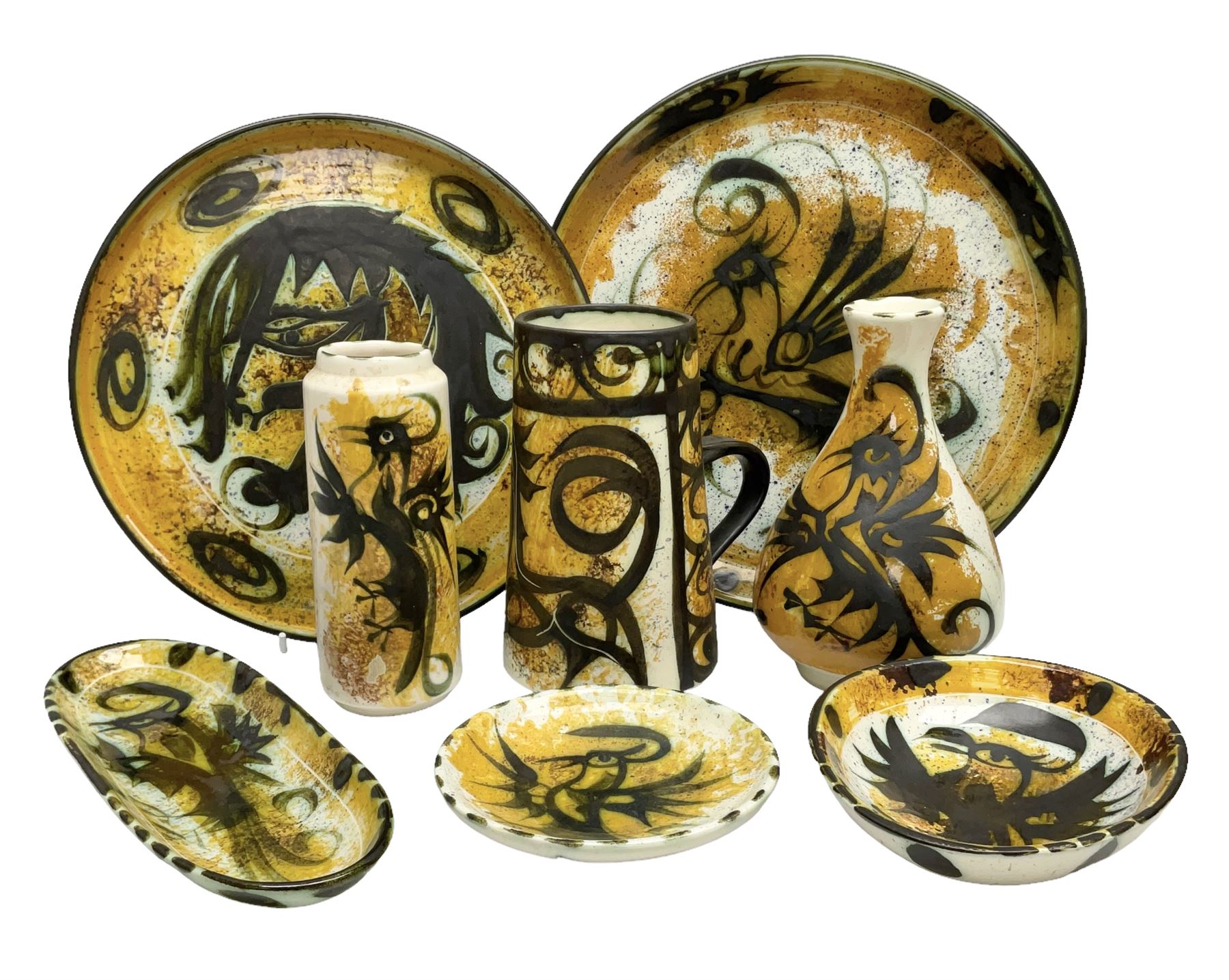 20th century Celtic Pottery, Newlyn, vases of baluster and cylindrical form, ovoid shaped bowl, plates, rectangular shallow dish etc, all decorated with a dark stylised phoenix, modelled with wings outstretched upon sponged ochre, blue and cream ground, together with a plate decorated with a stylised horse and tankard of tapering form (8)