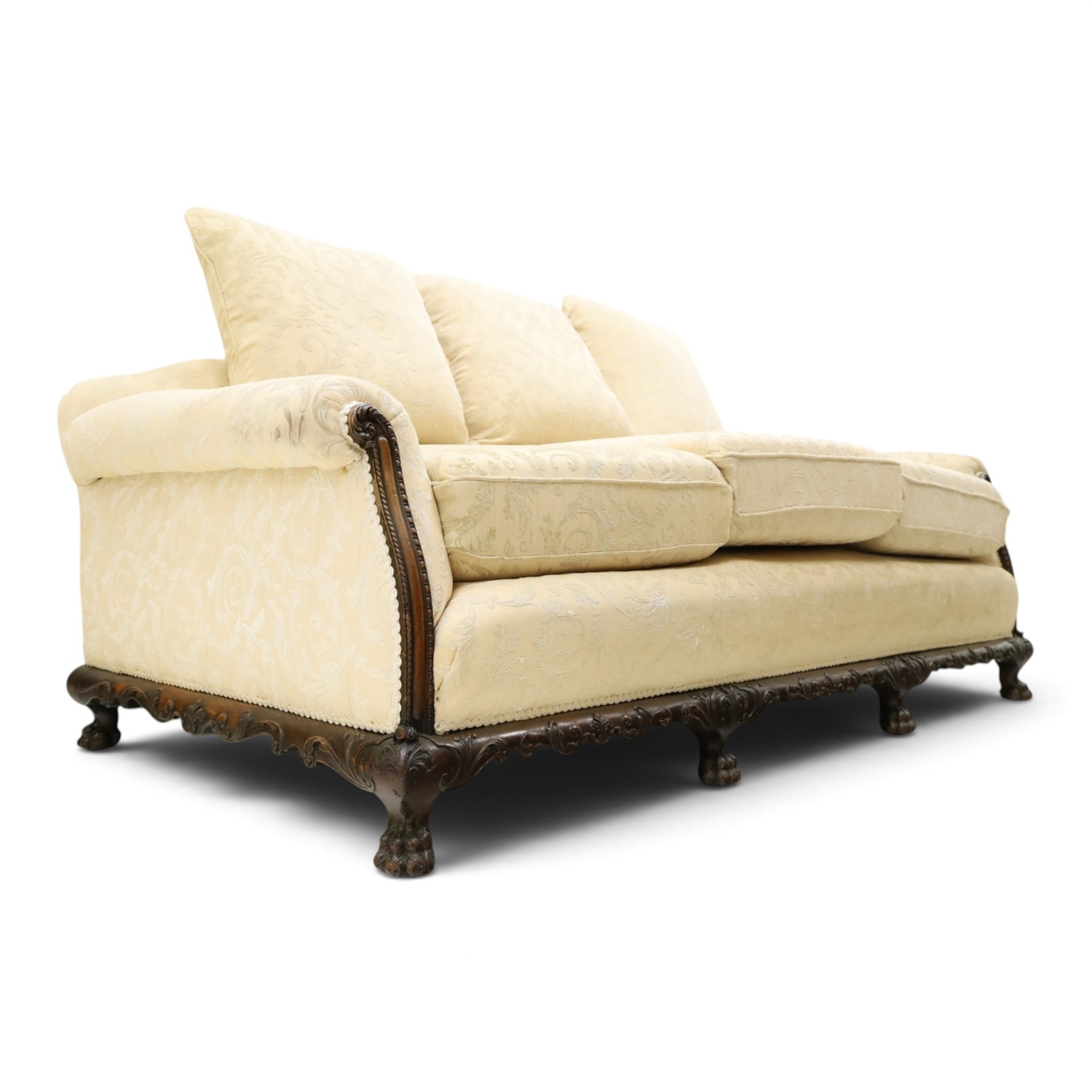 Quality Edwardian carved mahogany lounge suite comprising three-seater settee and pair of armchairs, the sofa with arched back over rolled arms and deep sprung seat, the arm terminals carved with acanthus rosette over gadroon and rope-twist moulding, the shaped apron carved and moulded with scrolling foliate acanthus motifs, terminating to four large front hairy paw and ball feet, upholstered in pale yellow foliate fabric with matching seat and scatter cushions (W200cm D105cm H73cm); the matching deep armchairs (W78cm D95cm H75cm)