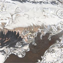 Edwardian silver mounted stationery box and silver mounted blotter, the box of rectangular form with curved front with applied repousse silver panels of putti within a scrolling foliate edge, the hinged cover opening to reveal an emerald green silk lined interior, the blotter with conforming silver mounted panels, each hallmarked William Comyns & Sons, London 1901, box H20cm W31cm D14cm, blotter H32cm W26.5cm