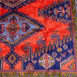 West Persian Veis hand-knotted rug, coral red field decorated with a series of bold geometric lozenge medallions in shades of indigo and sky blue surrounded by angular tribal motifs and stylized animal and plant forms framed by a deep indigo border of geometric ornament and multiple guard stripes, cotton fringe ends 