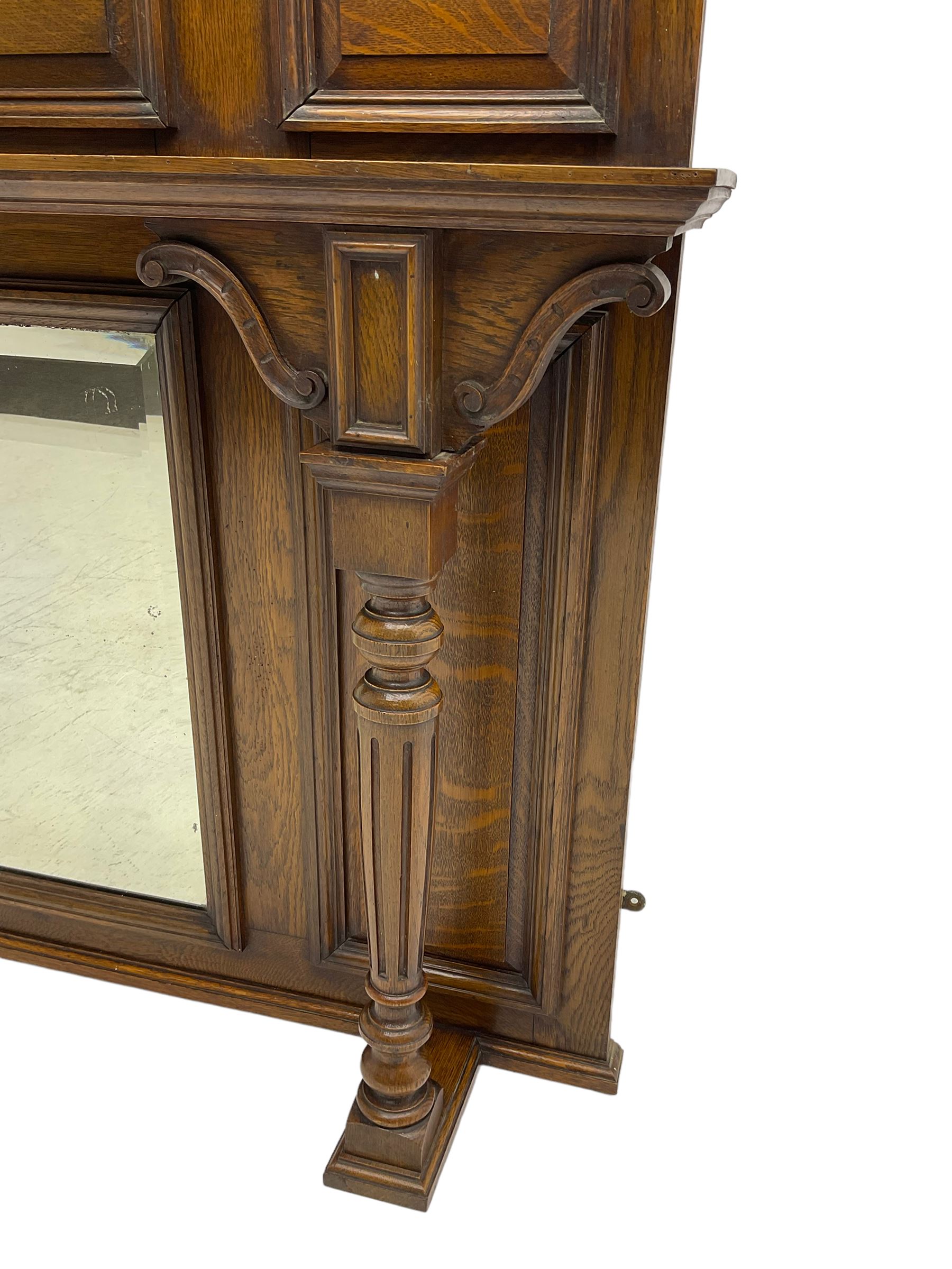 Oak overmantle mirror, arched pediment carved with shield and flanking fish with trailing scrollwork, panelled frieze over extending canopy raised by turned and fluted column pilasters, bevelled mirror plate 