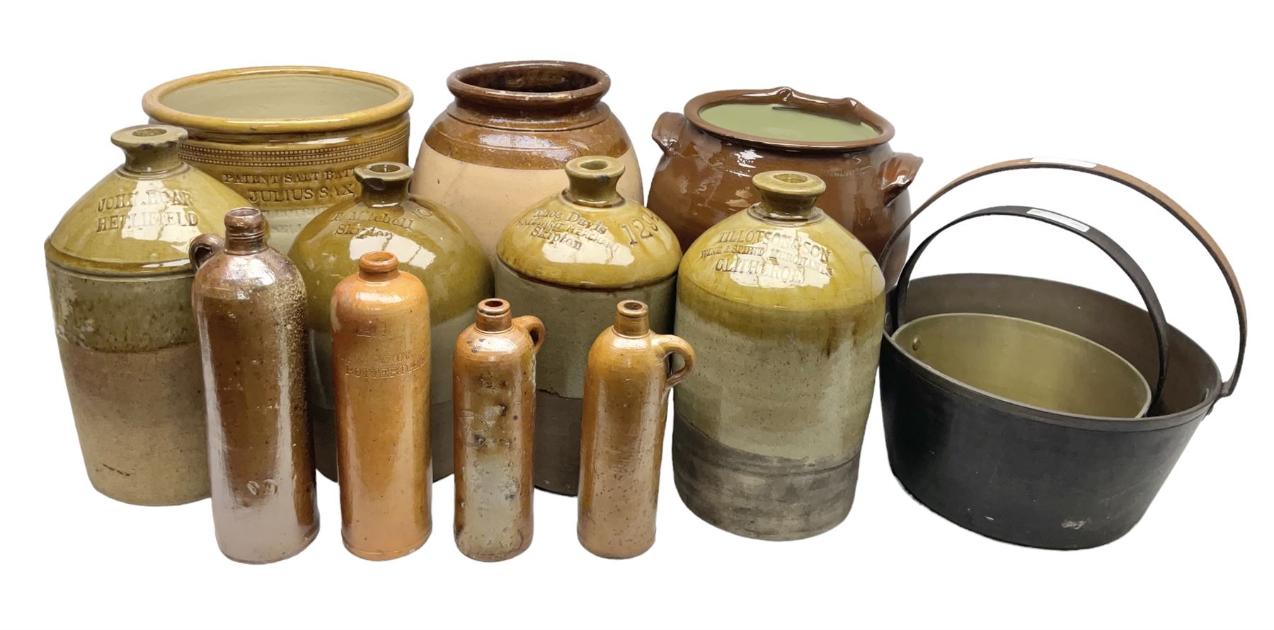Quantity of stoneware flagons, to include Skipton, Clitheroe and Hellifield related examples, four salt glazed bottles, large cylindrical stoneware jar, large twin handled jar and vase, together with two brass jam pans, tallest H35cm