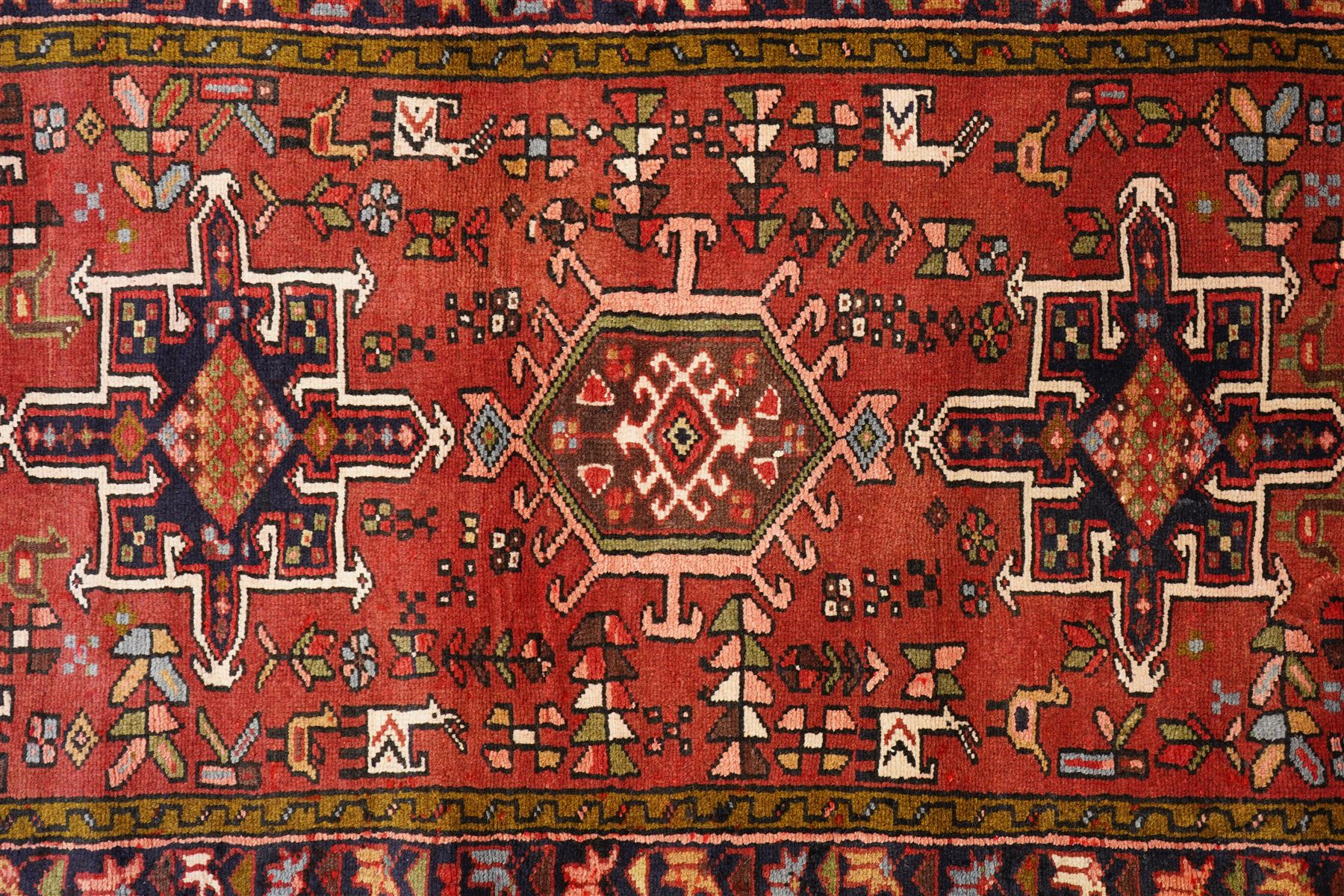 North West Persian Karajeh hand-knotted runner, madder red field with a series of shaped hexagonal medallions and cruciform motifs each enclosing geometric rosette devices linked by angular vine elements, field populated with stylized tribal ornaments, within narrow multiple borders decorated with repeating angular motifs framed by guard stripes of geometric devices, with cotton fringe ends  