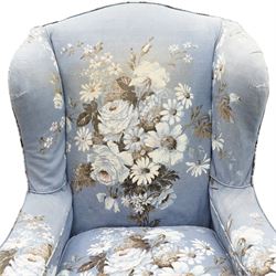 Pair of Queen Anne wingback armchairs, high back over out-swept arms, raised on ball-and-claw feet, upholstered in sky-blue ground floral chintz loose upholstery with pleated skirt and squab cushion