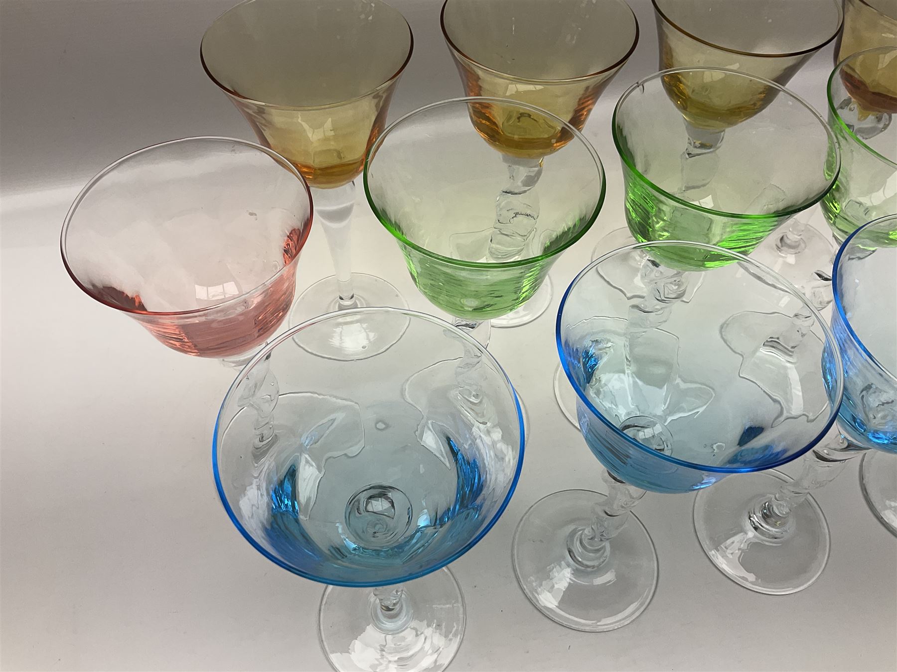 Ten coloured Adriana wine glasses by Abigails, to include blue, green, pink and yellow examples, each with part faceted bowl and twist stems, together with two similar orange examples with pulled stems, H24cm