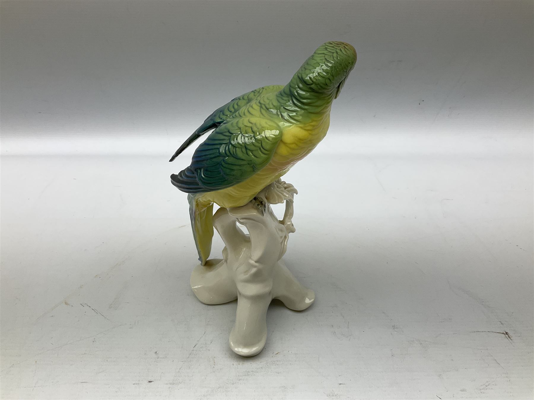 Karl Ens porcelain figure of a parrot, modelled with yellow breast, blue back and wings and green tail, perched upon on a blossoming branch, with blue printed factory mark beneath, H24.5cm