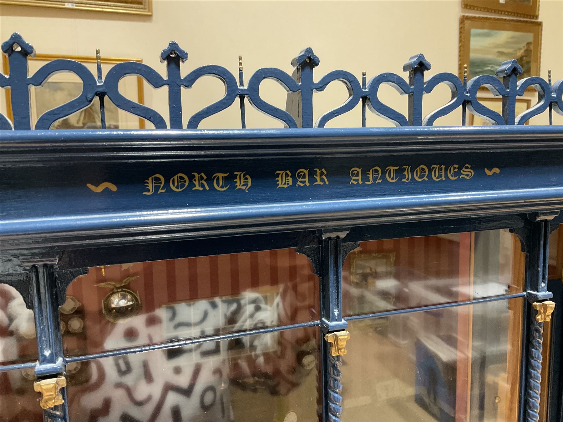 Good quality late 20th century dolls house by M. James dated 1995 in the form of a Beverley East Yorkshire Antique Shop called 'North Bar Antiques'; single-storey single-roomed shop with textured brick walls and flat roof, fully glazed hinged front with recessed hinged customer door and central window to the rear; comprehensively furnished with chests of drawers, pedestal desk, breakfast table, lowboy, two longcase clocks, delft rack with ceramics, occasional tables, pictures, Regency style mirror and collectibles; decorated walls with coving and picture rail and simulated floorboarding; wired for electric lighting; maker's plaque W61cm H42.5cm D41.5cm