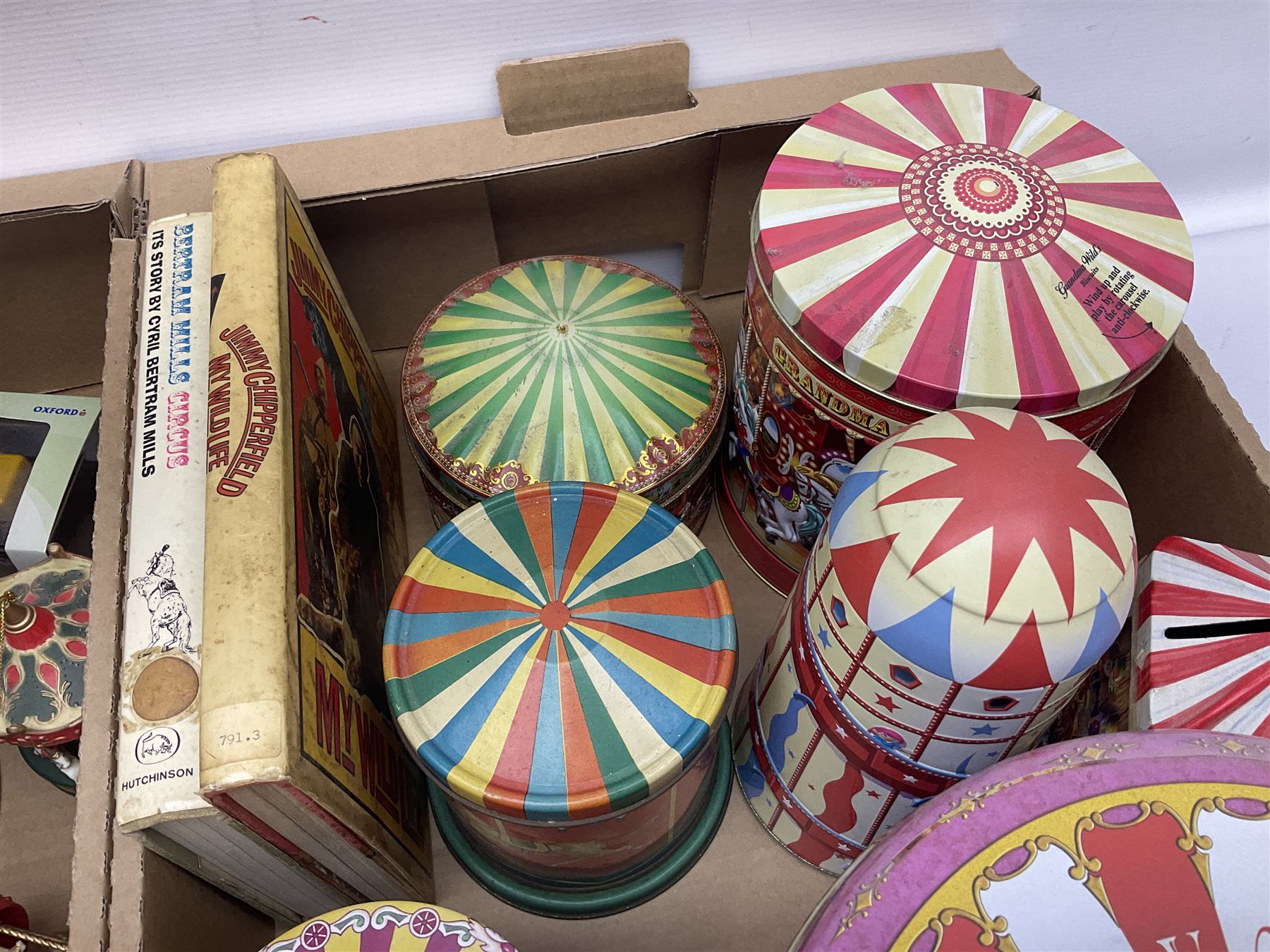 Collection of circus and fairground collectables, to include teapots, biscuit tins, including musical examples, and four Circus/fair themed books, including two library first editions