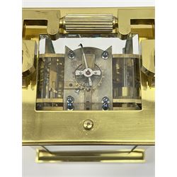 Early 20th century brass and bevelled glass repeater carriage clock with alarm, the angular and cylindrical ribbed handle and repeater button over stepped cavetto cornice, white enamel Roman dial with Arabic subsidiary alarm set dial, twin train eight day movement striking the hours and half on coil, separate alarm mechanism train, stepped moulded and plain faced base, with leather travelling case