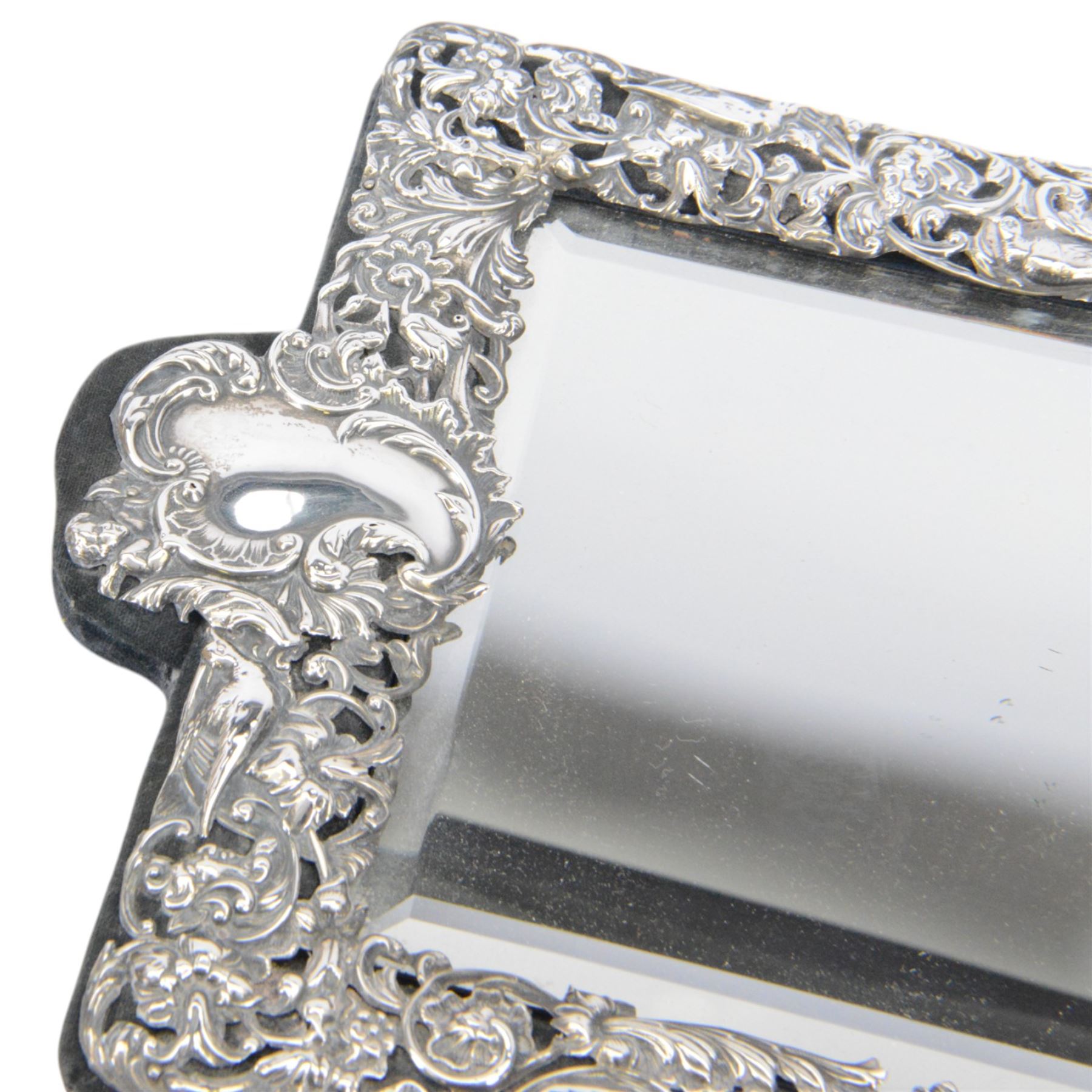 Edwardian silver mounted dressing table mirror, the bevelled mirror plate with silver surround embossed with flowers, C scrolls, putti and birds, with velvet easel support verso, hallmarked London 1903, maker's mark WC, probably for William Comyns & Sons, H33cm