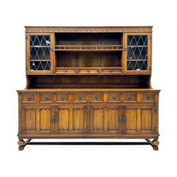 Large mid-20th-century oak dresser with two astragal glazed doors between gallery shelf and lower shelf, with three short drawers and lower section with four drawers and three double-panelled linen-fold hinged cupboard doors 