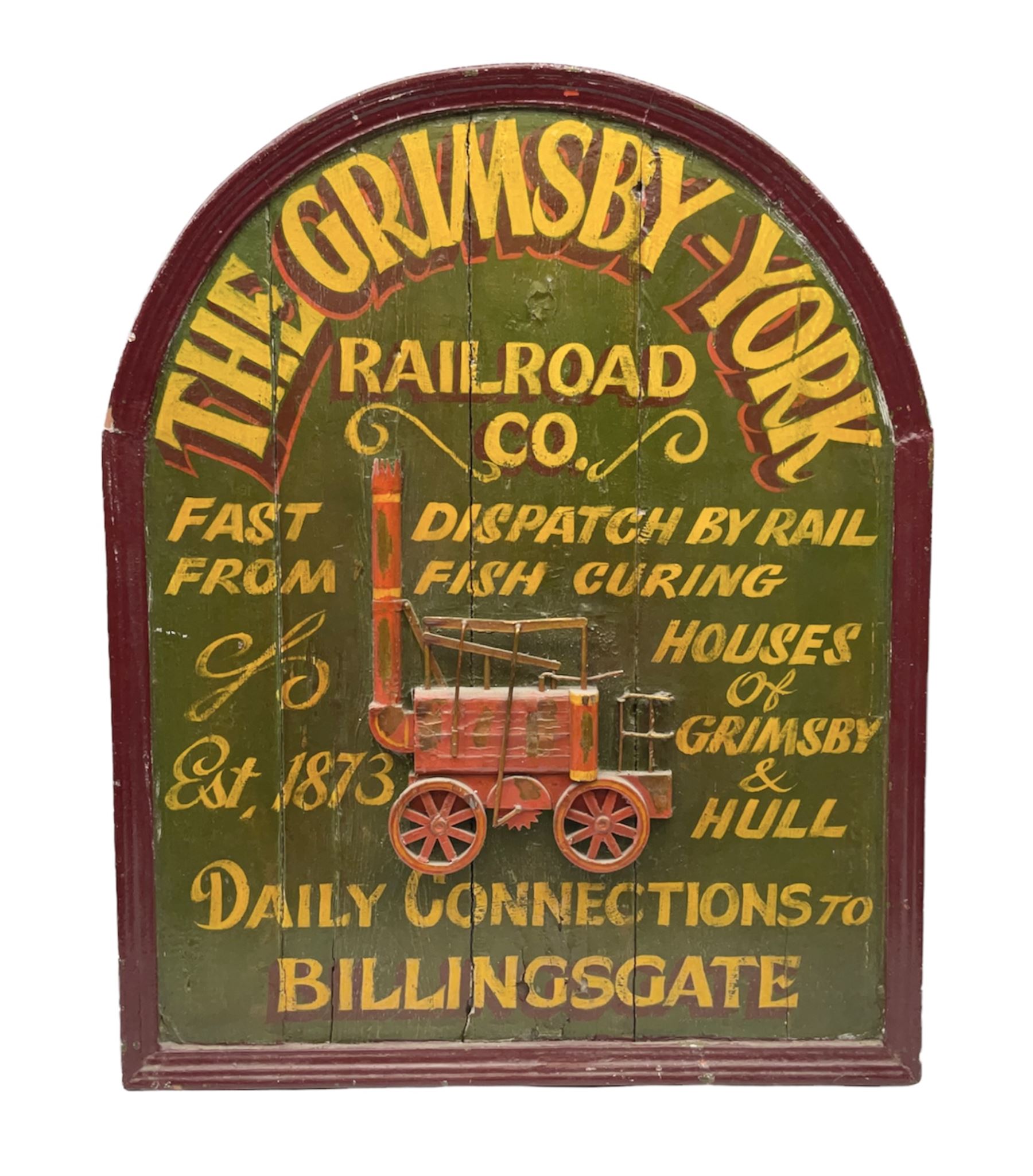 `The Grimsby-York Railroad Co.` painted wooden railway advertising sign 20th century, of planked construction with arched top and moulded border, decorated with an applied wood and metal image of an early steam locomotive in relief, the surrounding wording reading `The Grimsby-York Railroad Co., Fast Dispatch by Rail from Fish Curing Houses of Grimsby & Hull, Est. 1873, Daily Connections to Billingsgate`, 89 x 71cm

