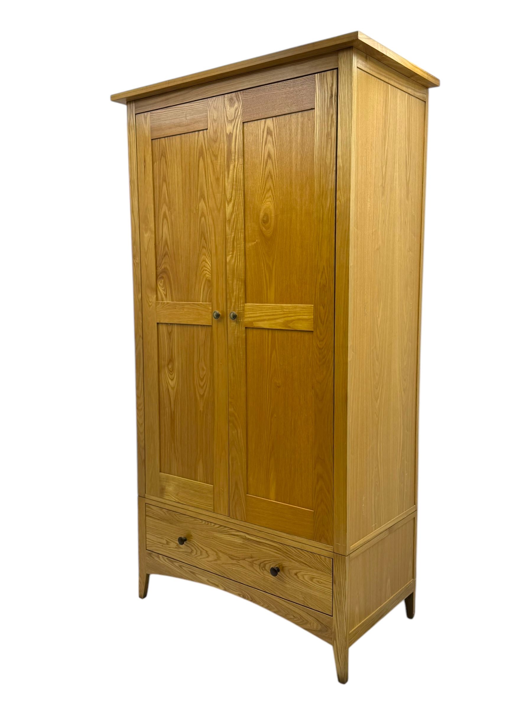 Contemporary light oak double wardrobe, projecting cornice over two panelled doors enclosing hanging rail and shelf, above full-width drawer, on shaped stile supports
