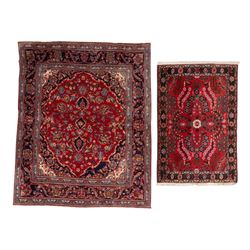 Two Persian rugs, the larger with a crimson field decorated with three linked indigo medal...