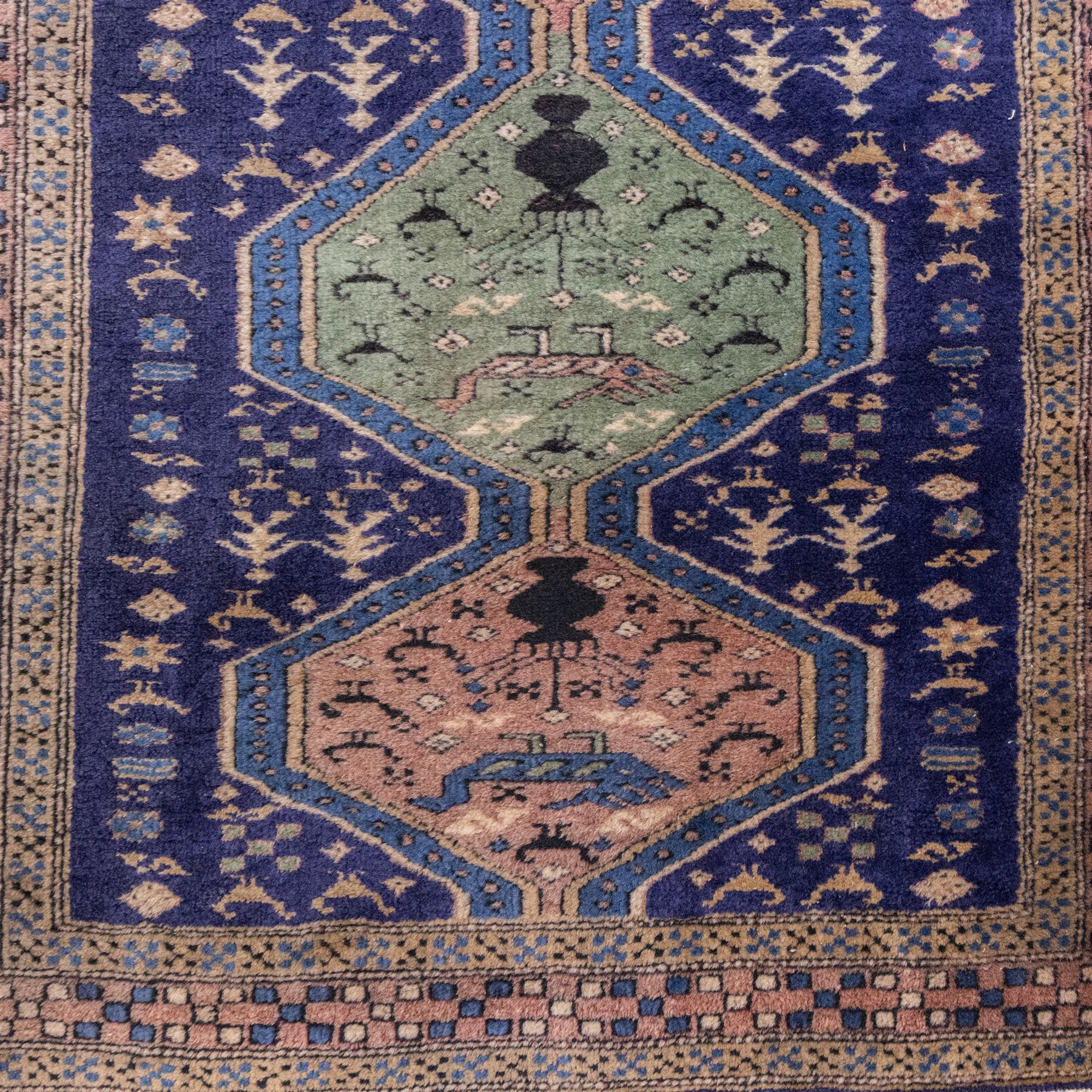 North West Persian Ardebil hand-knotted runner, indigo field composed of a vertical series of large linked hexagonal medallions alternating soft terracotta and sage-green grounds, medallions connected narrow waist panels, surround field filled with geometric devices on a pale blue ground, principal border decorated with a repeating geometric and floral motif on a light ground flanked by narrow guard stripes incorporating small rosettes, with cotton fringe ends 