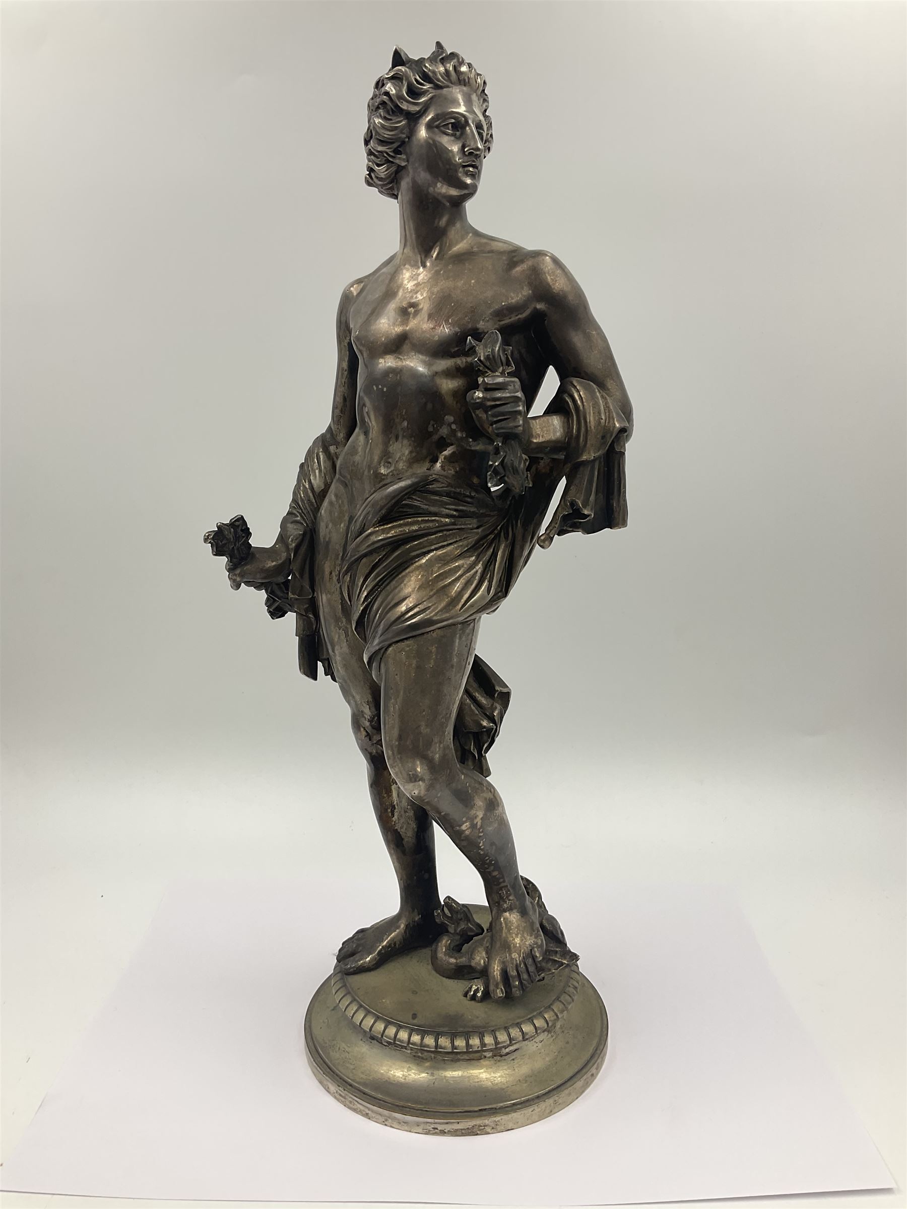 20th century silver plated figure, modelled as a classical male figure, possibly Prometheus, holding flames, one foot resting atop a small dragon, upon a circular spreading base, overall H37.5cm
