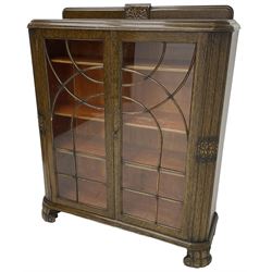 Early 20th century oak bookcase or display cabinet, raised back with carved floral decoration, fitted with two astragal glazed doors enclosing three adjustable shelves, on scroll feet
