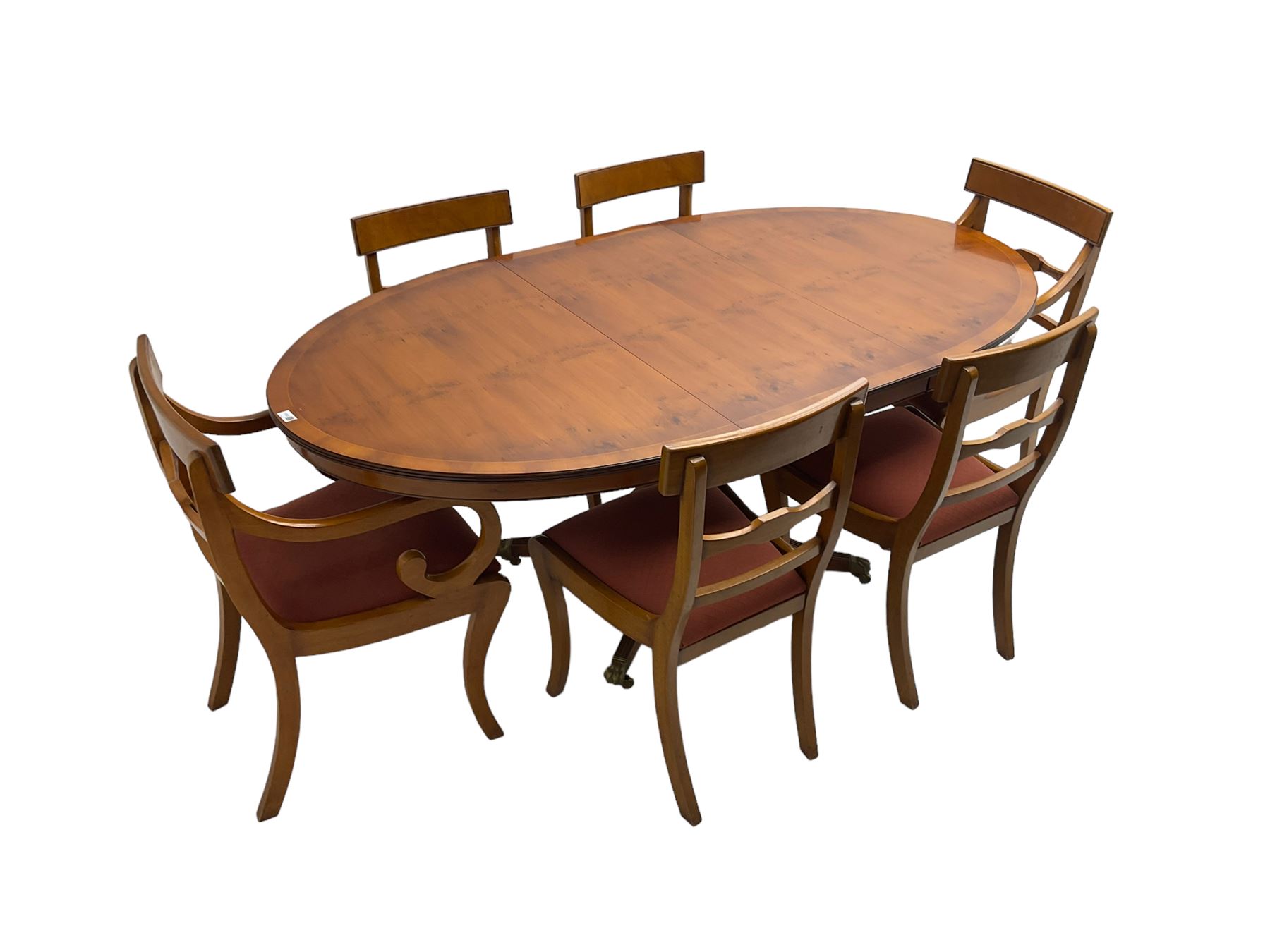 Regency design yew wood dining table, oval cross-banded top with reeded edge, raised on turned pedestal with reeded sabre supports terminating in brass hairy paw feet and castors (W138cm D100cm H75cm); and Rackstraw - set six (4+2) Regency design dining chairs with red drop-in seats (W50cm H86cm)