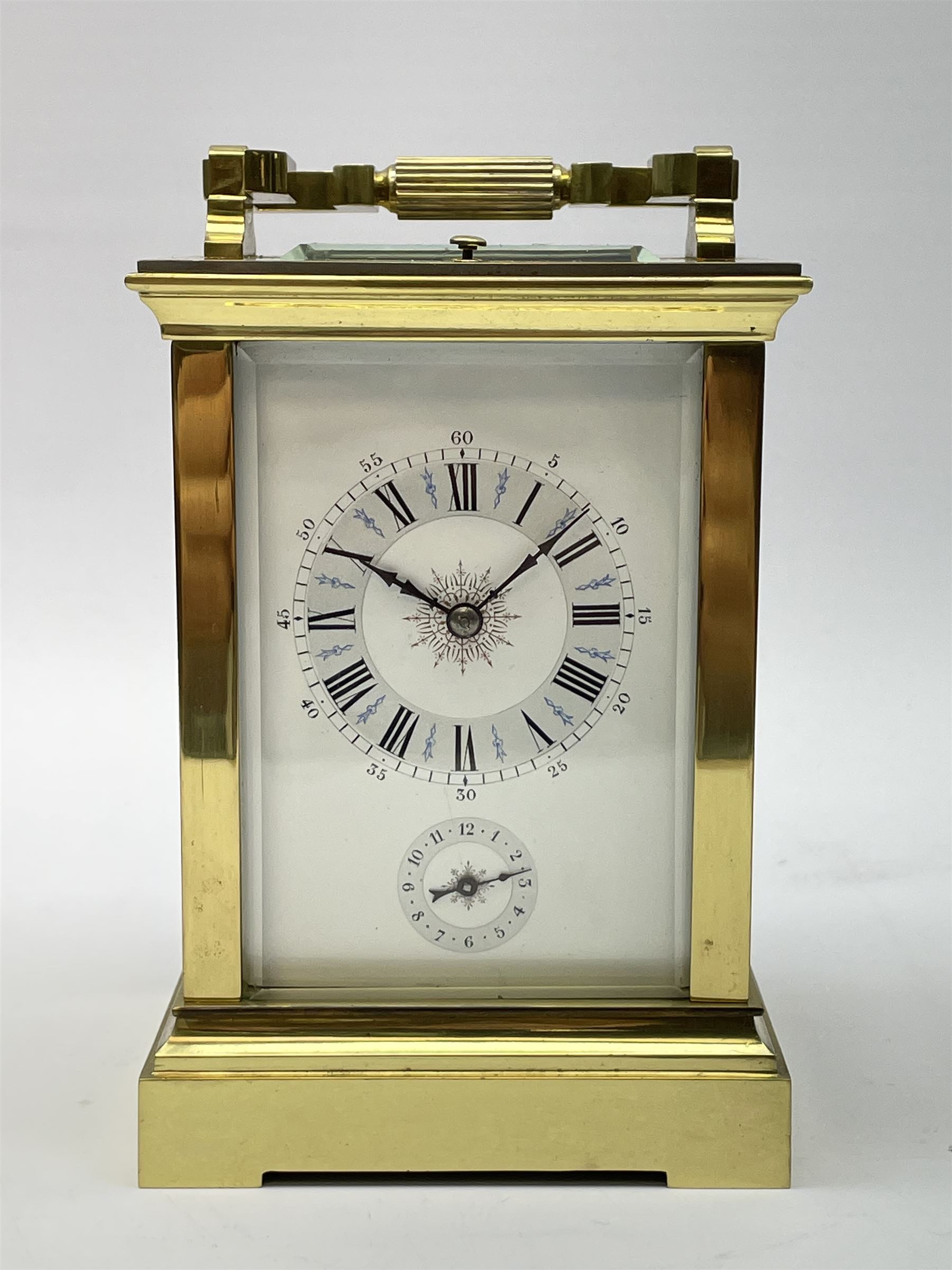 Early 20th century brass and bevelled glass repeater carriage clock with alarm, the angular and cylindrical ribbed handle and repeater button over stepped cavetto cornice, white enamel Roman dial with Arabic subsidiary alarm set dial, twin train eight day movement striking the hours and half on coil, separate alarm mechanism train, stepped moulded and plain faced base, with leather travelling case