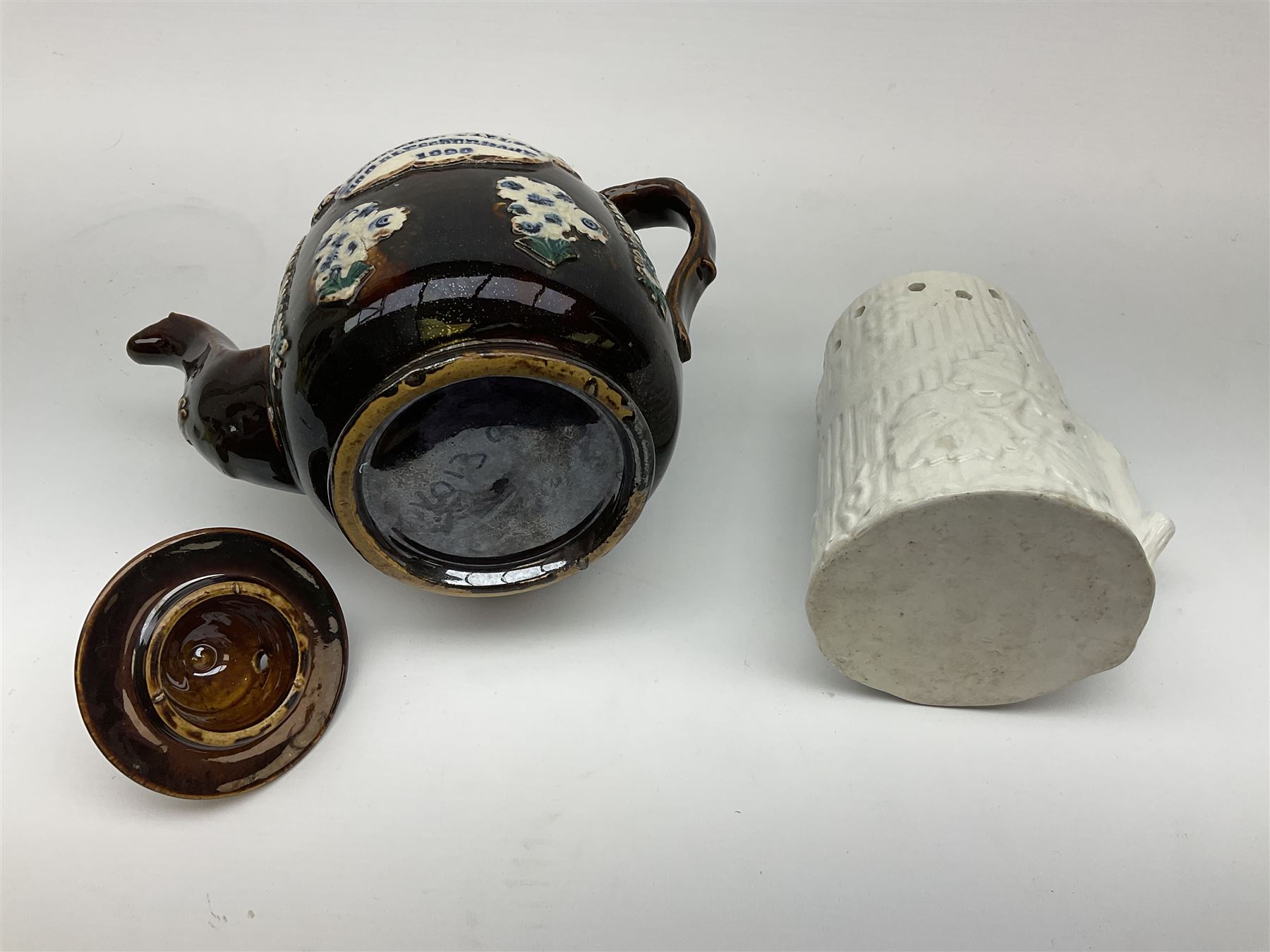 A 19th century Barge Ware teapot, decorated with applied floral sprays and thistles against a mottled brown ground, and plaque detailed Catherine Taylor God Bless Our Home 1890, H18cm, together with a white glazed puzzle mug, H15cm. 