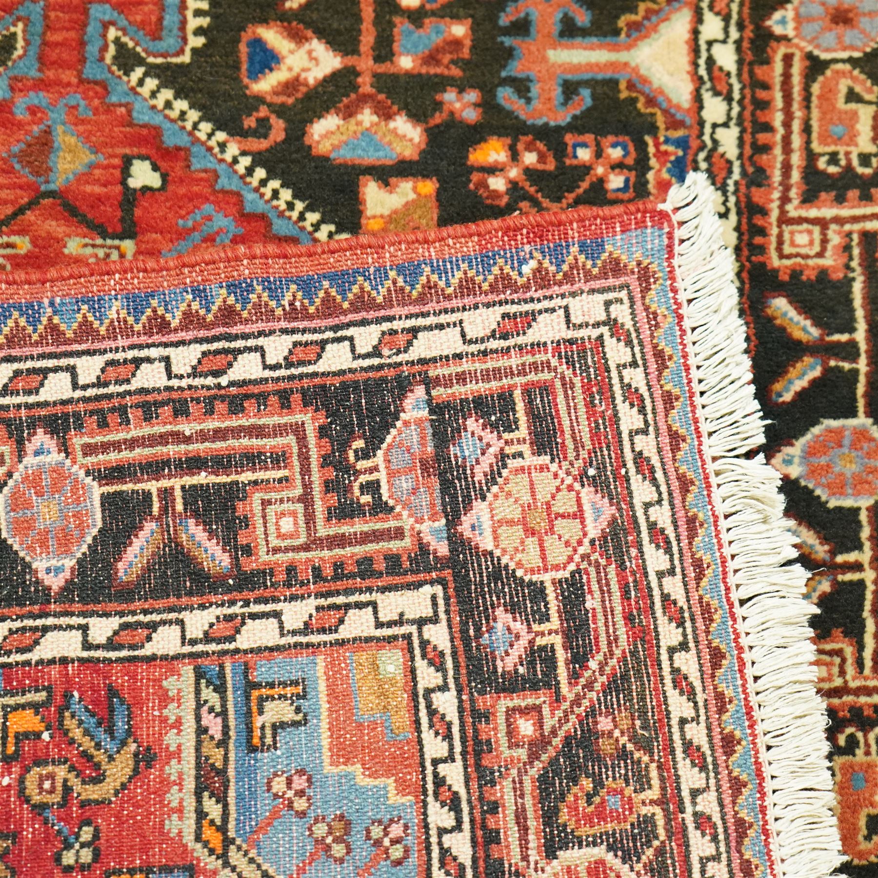 North West Persian Heriz hand-knotted rug, indigo and madder red field with a central angular medallion with stylized floral and geometric motifs within multiple patterned borders with fringe ends 