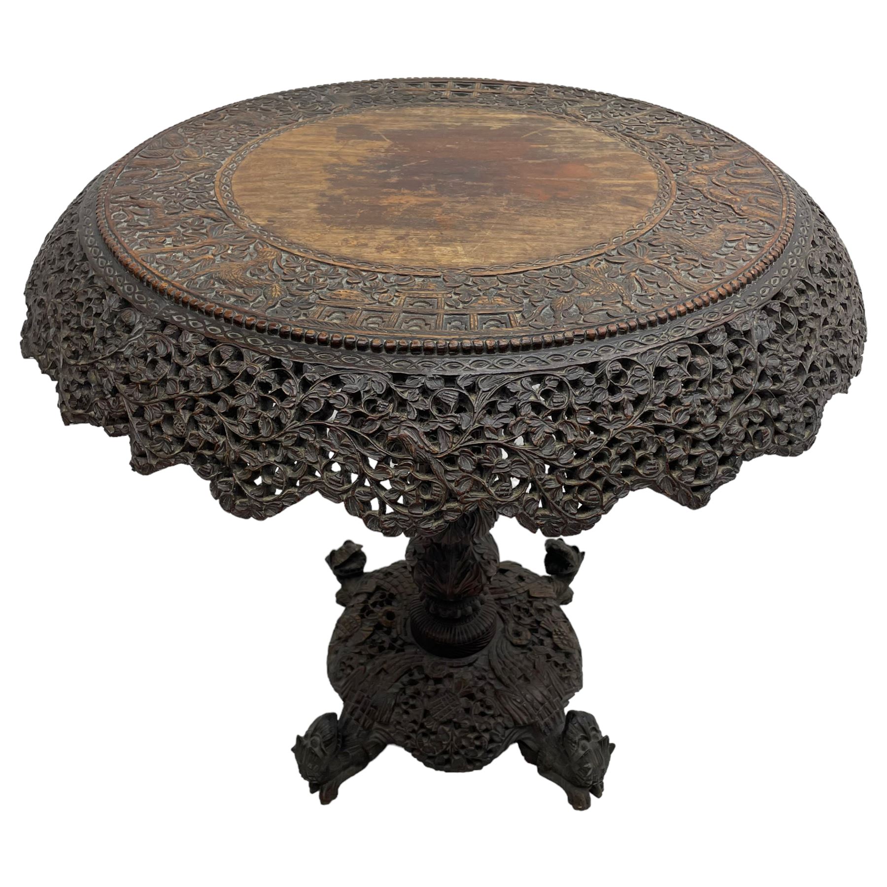 Late 19th century Anglo-Indian carved hardwood occasional table, circular tilt-top carved profusely with mythical animals and foliage decoration, pierced and carved with interlaced leafy branches, leaf carved pedestal supports on a raised platform with further carved and pierced foliage decoration, four carved feet in the form of mythical beasts with gaping jaws 