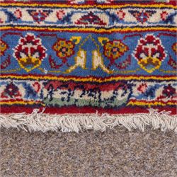 Central Persian Kashan hand-knotted carpet, madder red field with central cusped medallion in navy and ivory enclosing a floral rosette and radiating scrolling arabesques and palmettes, across a densely ornamented ground of finely drawn vinery enriched with a profusion of flowering sprays and stylized blossoms, spandrels in deep indigo and principal border of navy ground decorated with a continuous palmette and vine-scroll flanked by multiple guard stripes, with cotton fringe ends