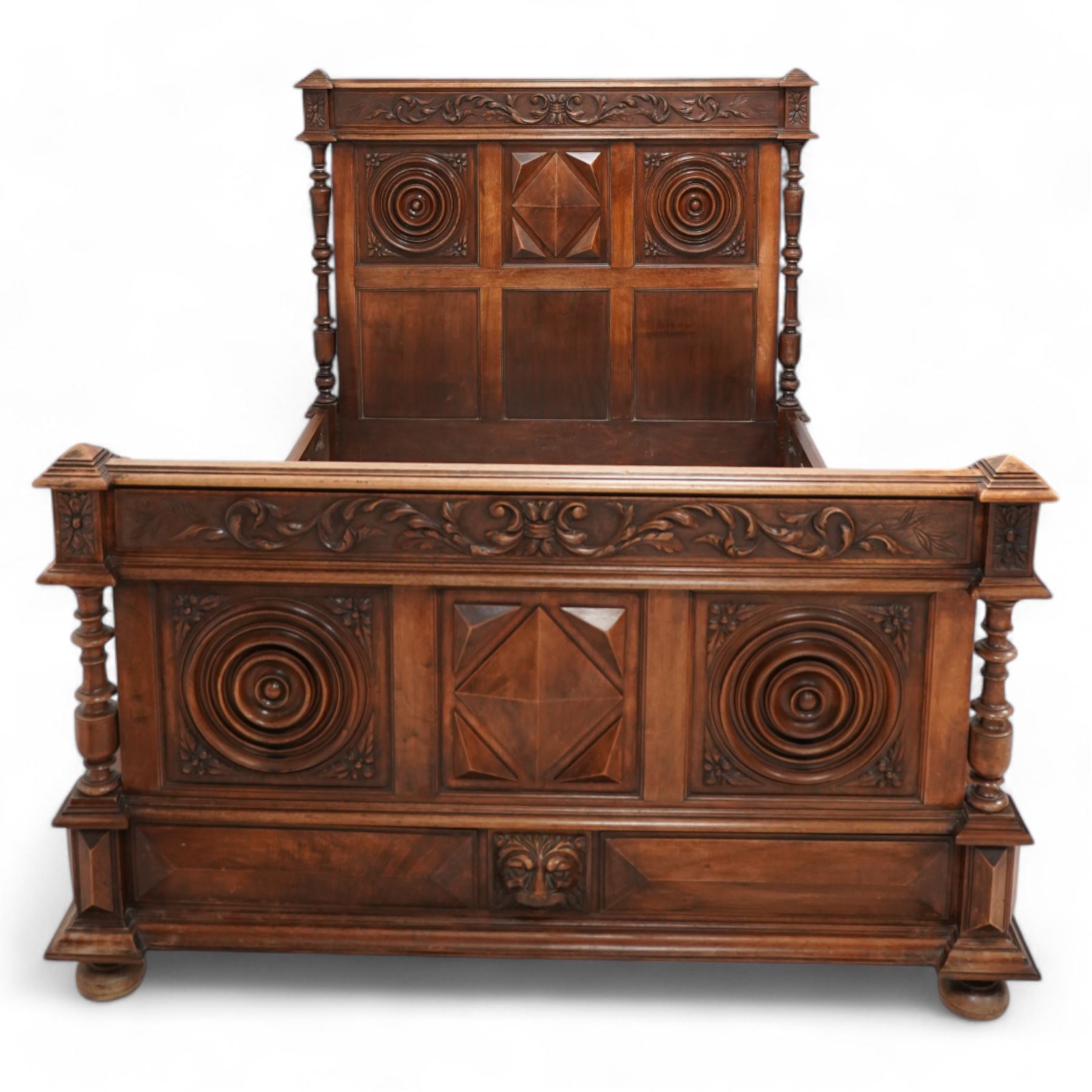Late 19th century French walnut double bedstead, the panelled headboard with curling foliage carved frieze over concentric turned roundels and faceted mounts, lion mask carved rails with applied panelled mounts, matching footboard with lower carved lion mask 