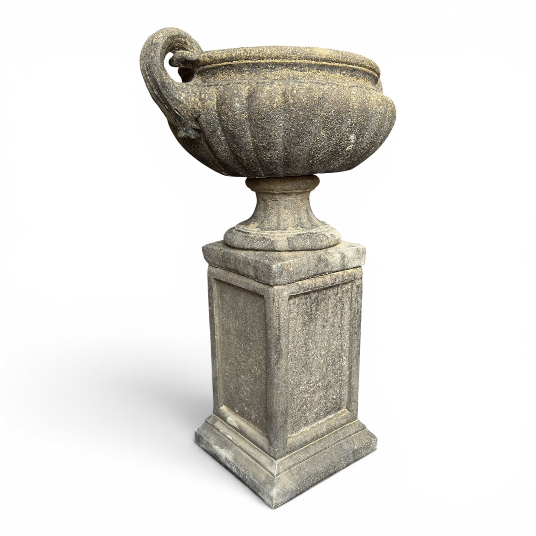 Pair of Neoclassical design weathered cast stone garden urns of kylix form, the rolled rim flanked by twin pierced scroll handles over a shallow gadrooned bowl, raised on a fluted circular socle and faux panelled square pedestal base