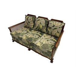 Early 20th century bergère lounge suite, mahogany framed with cane work back and sides, acanthus scroll carved uprights - three seat sofa (W167cm, H82cm, D83cm), and pair matching armchairs (W78cm), loose cushions upholstered in acanthus leaf scroll fabric with scatter cushions