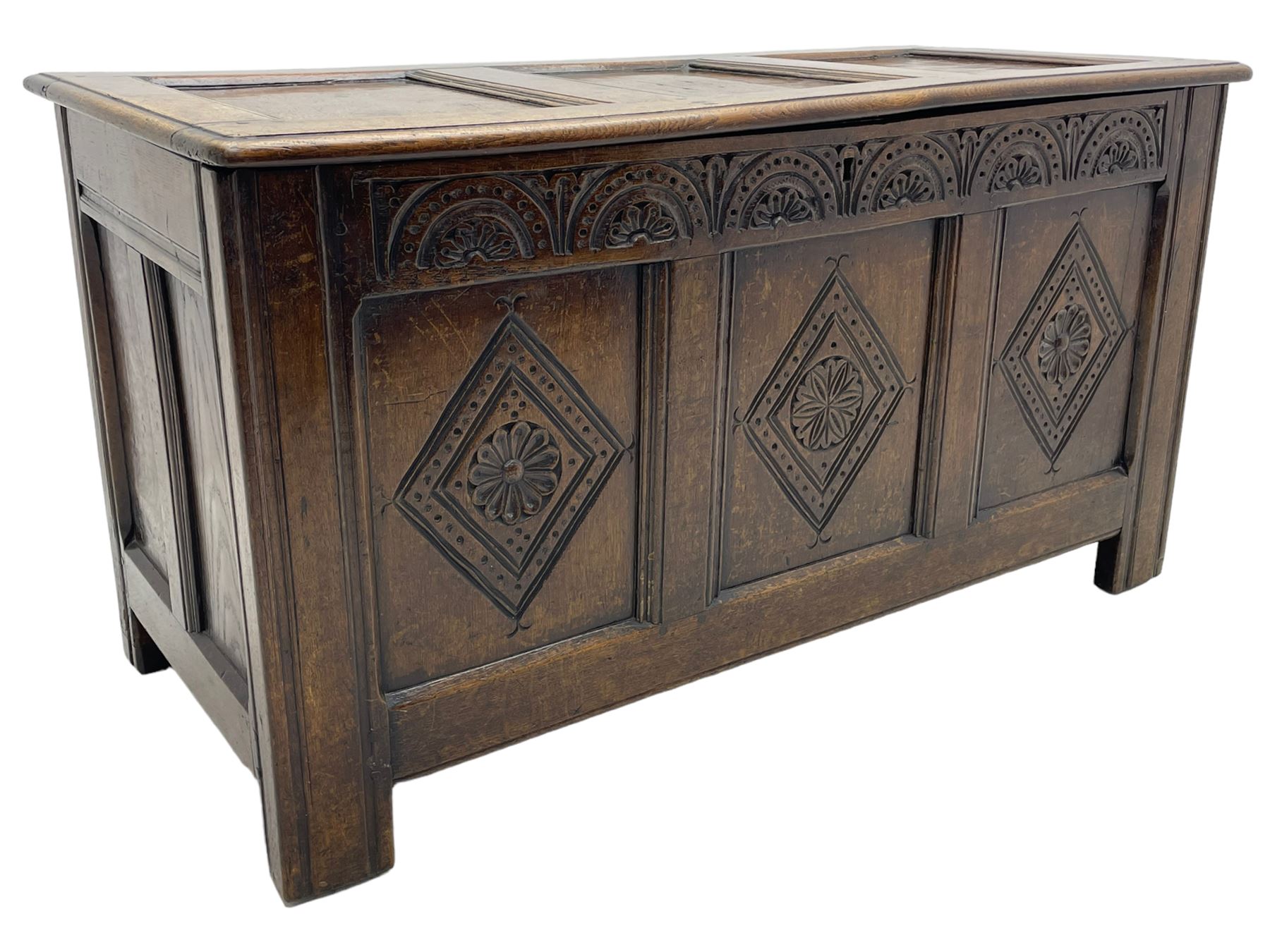 18th century oak coffer or chest, rectangular triple panelled hinged top with moulded edge enclosing main compartment and candle box, the frieze carved with repeating concentric lunettes and foliate patterns, the front fielded panels decorated with lozenges containing central flower heads, on stile supports