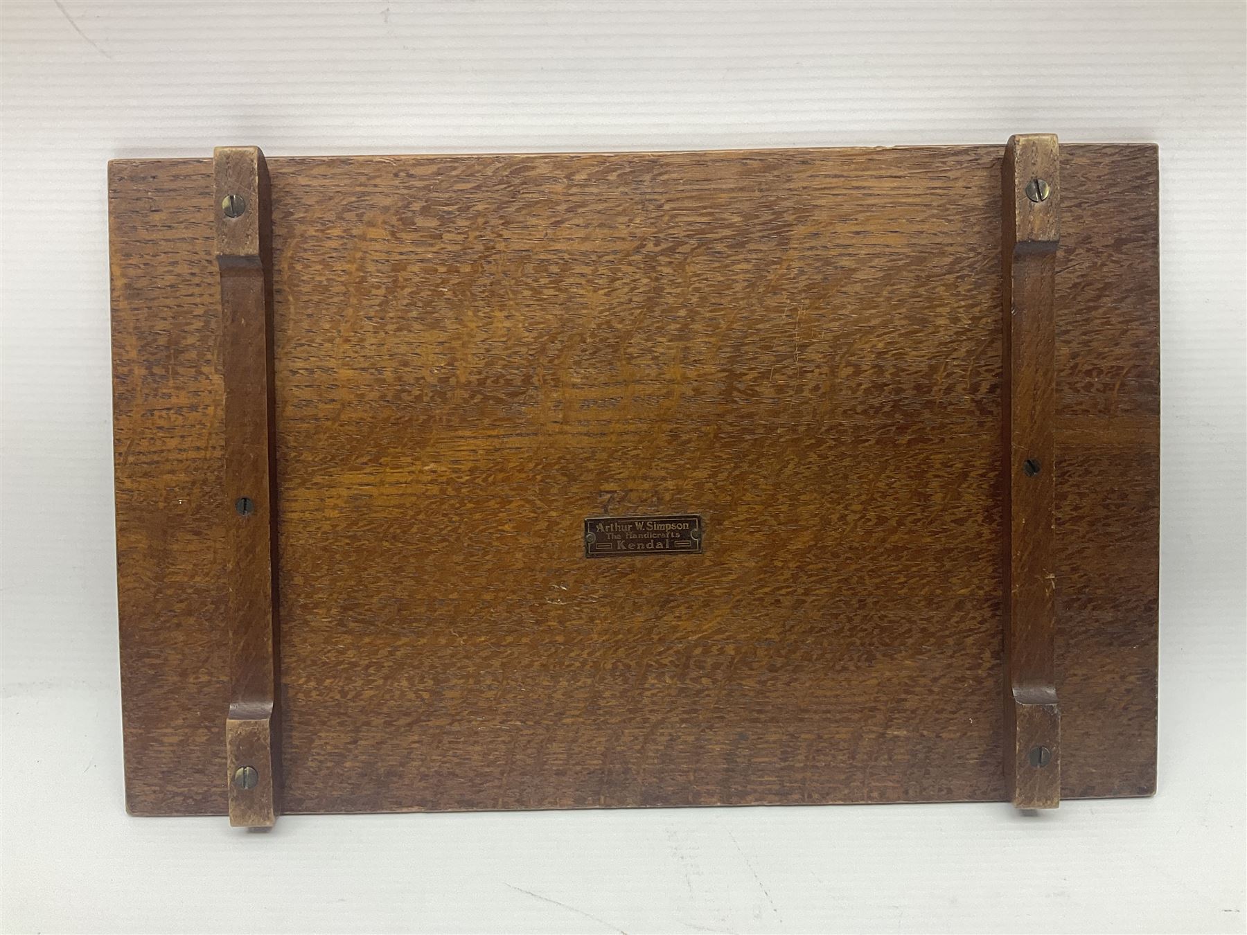 Arts and Crafts oak stand by Arthur Simpson of Kendal, of rectangular form with central hammered pewter panel, surrounded by a border with carved foliate corners, upon two bar supports, bearing label detailed 