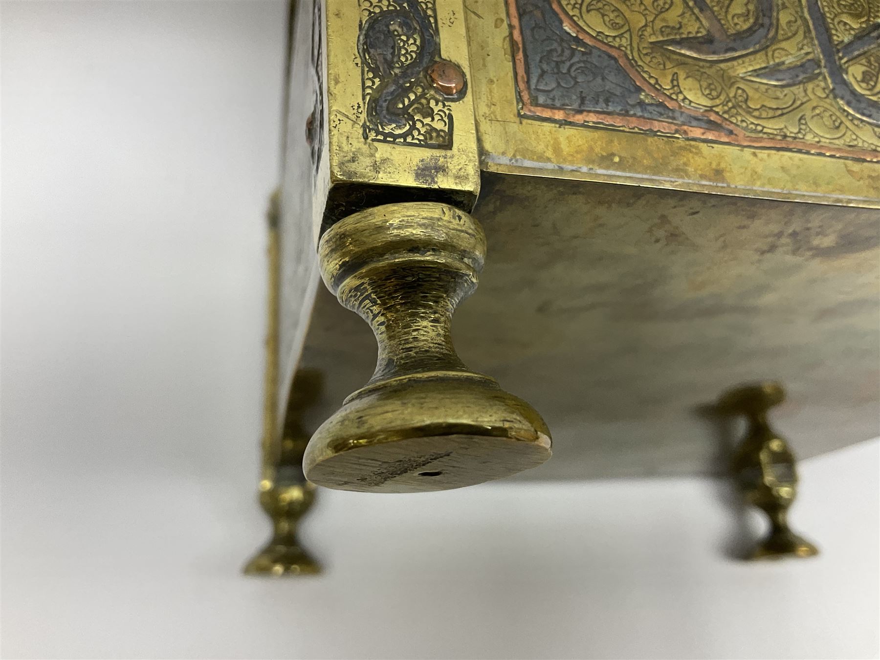 Late 19th century Damascus Cairoware Quran box, of square form with canted hinged cover, upon four circular pad feet, the brass exterior inlaid with silver and copper script and decorative detail, opening to reveal a marquetry lined interior, H15.5cm W19cm D19cm