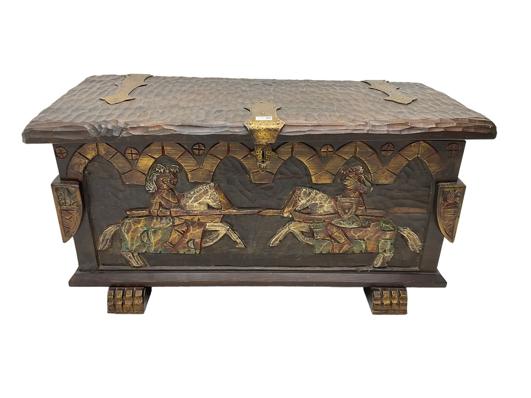 Carved wooden blanket chest, the tooled hinged lid with shaped metal strap hinges and catch, the front carved with arcade over two medieval jousters, on carved sledge feet