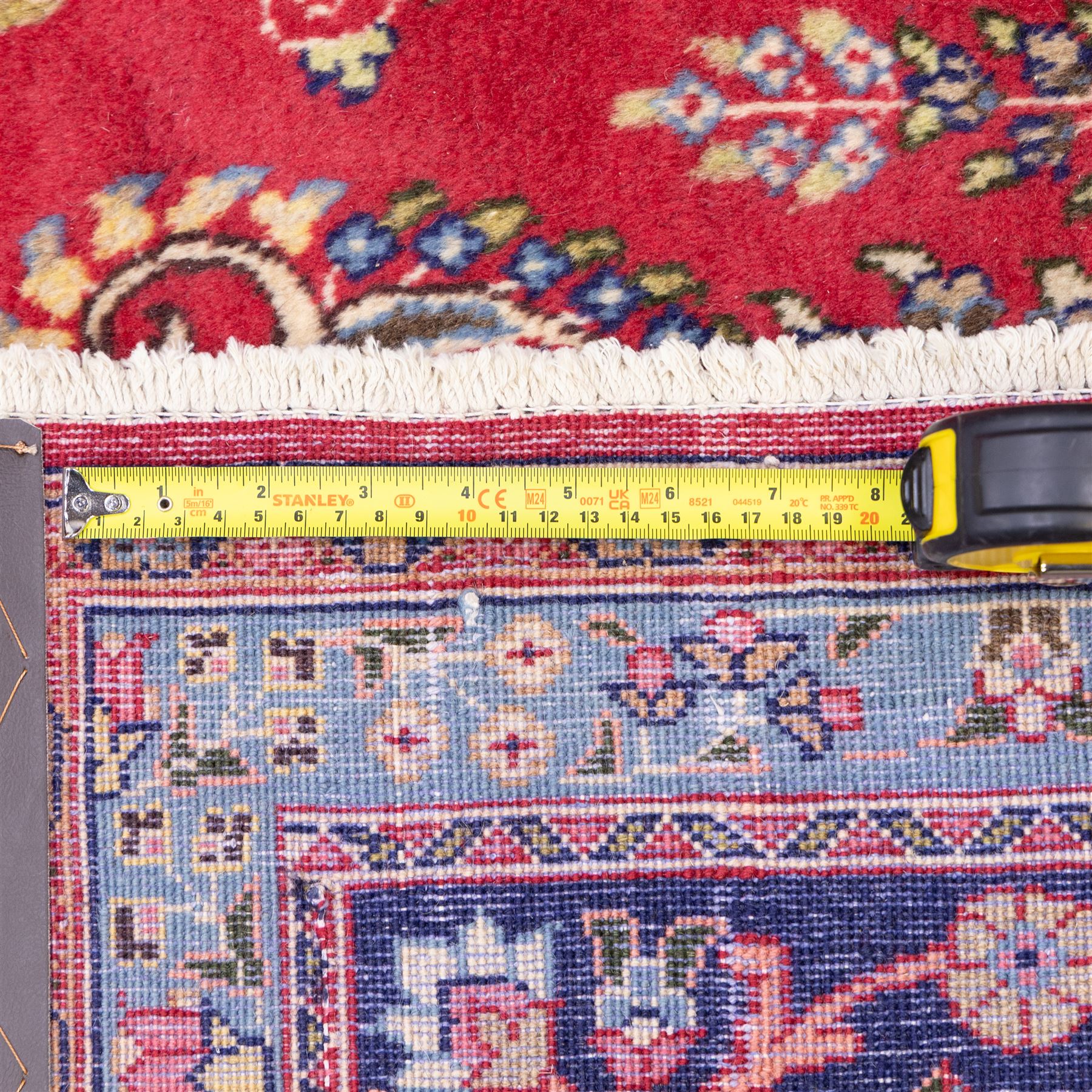 North East Persian Meshed hand-knotted rug, madder red field with central multi-lobbed medallion in shades of indigo, ivory, and sofa pastel tones surrounded by scrolling floral vines, palmettes, stylized blossoms, floral sprays, and cartouches, framed by Indigo spandrels, enclosed within a broad dark blue main border, flanked by multiple narrow guard stripes, with fringe ends 