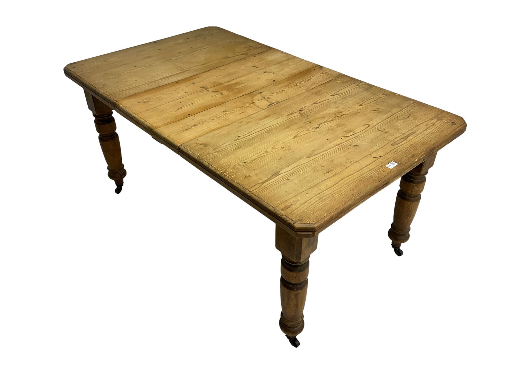 Late Victorian pine extending dining table, rectangular moulded top with canted corners and additional leaf, on turned supports with brass castors 