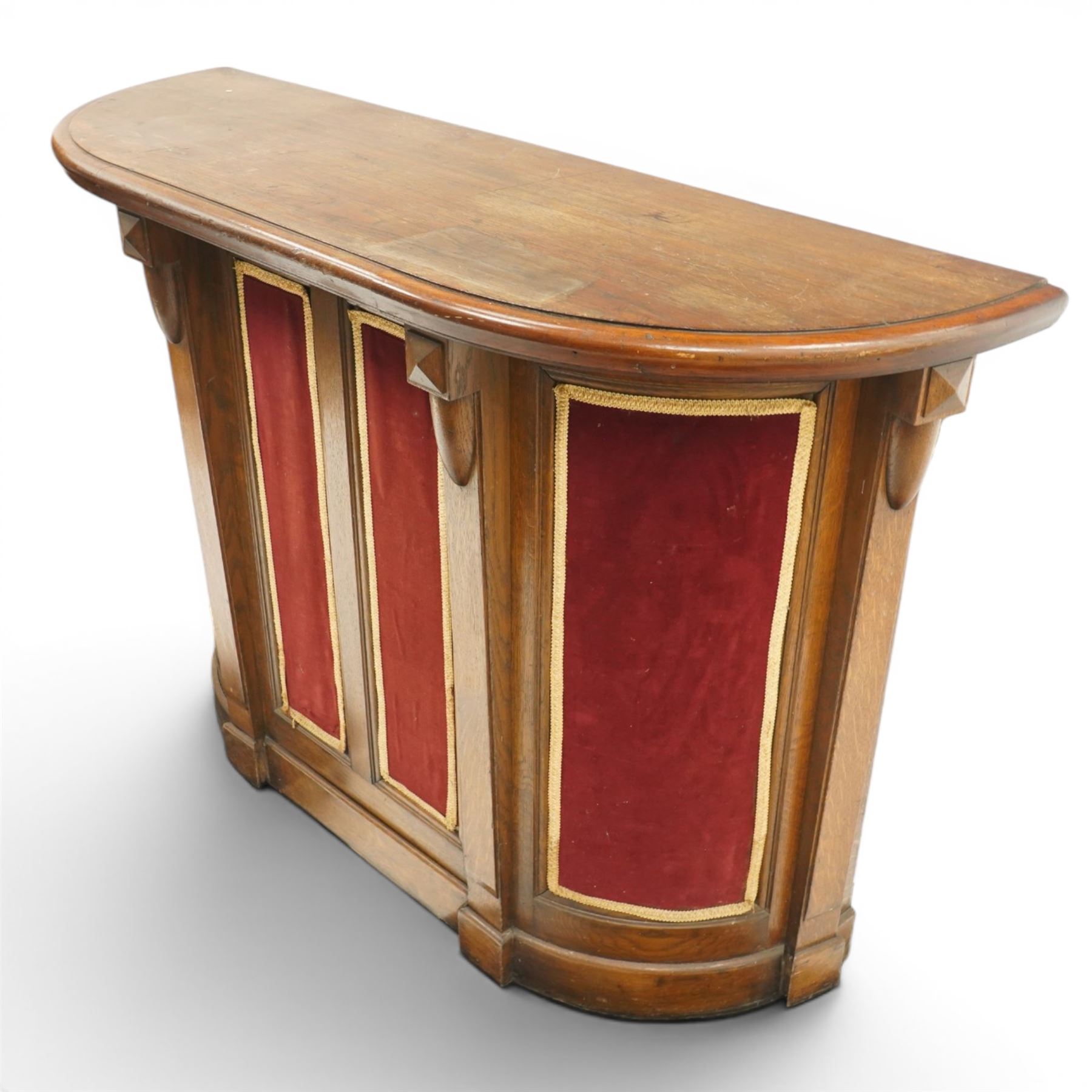 Arts & Crafts oak D-shaped bar, moulded edged counter above a front with velvet applied panels, the back with shelving, raised on a plinth base