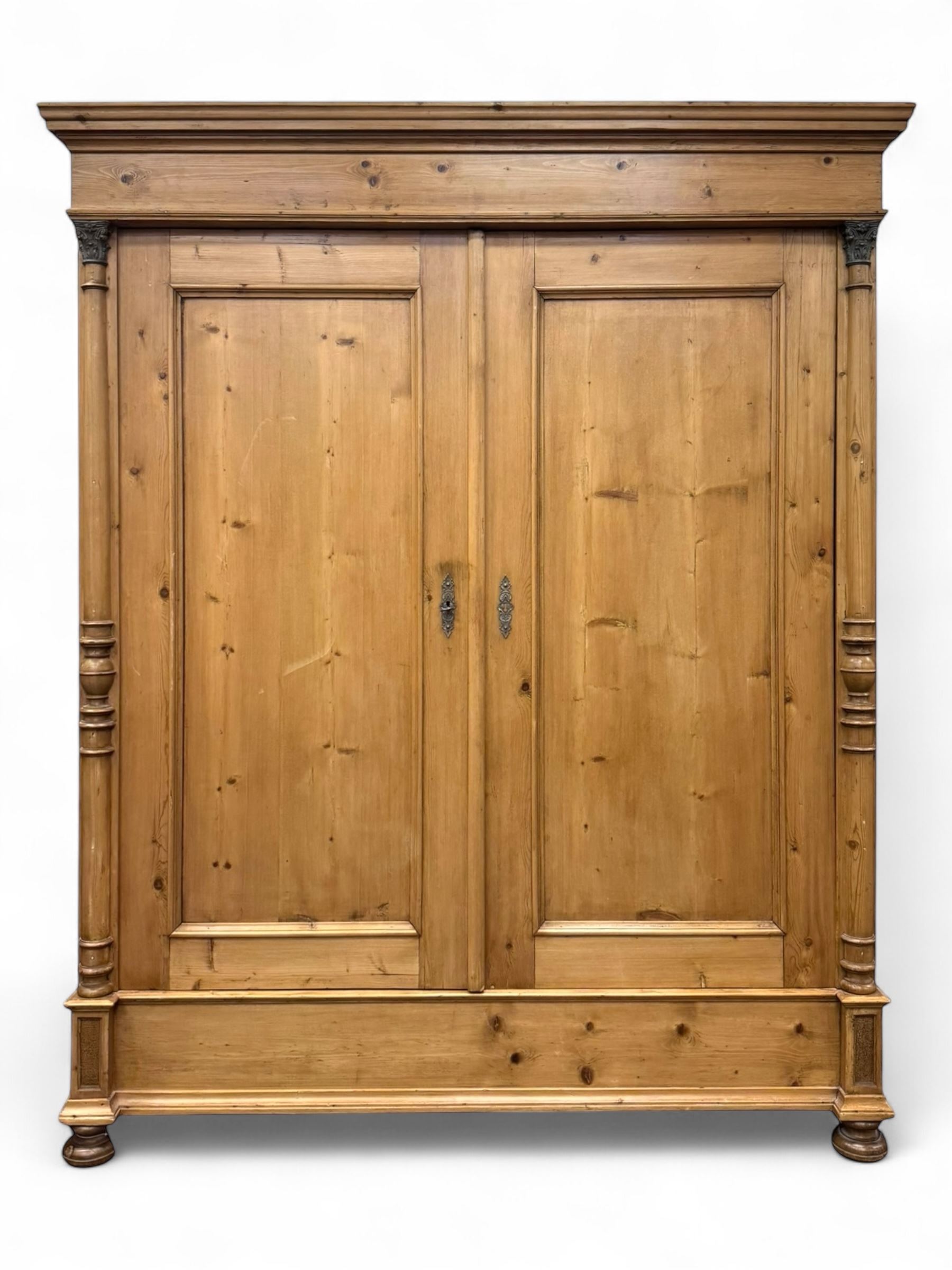 Large 19th-century Continental polished pine double wardrobe, panelled back and doors revealing brass hanging rod, flanked by half-turned columns with Corinthian capitals supported on bun feet