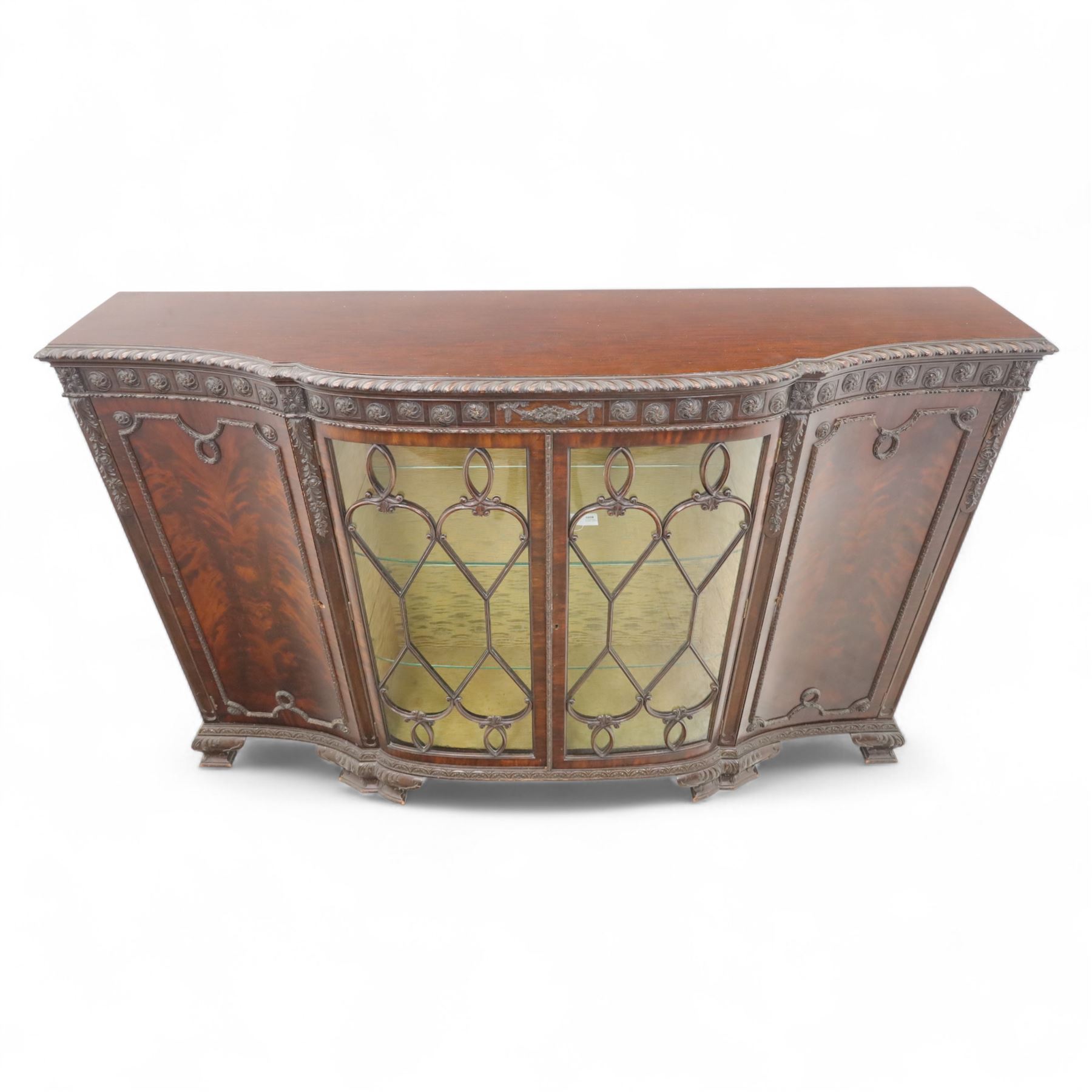 Edwardian mahogany serpentine breakfront display cabinet in the neoclassical style, the rectangular top above a carved frieze with roundels, foliage, and ribbon tied swags with central bow-fronted astragal glazed doors enclosing shelves, flanked by panelled doors, raised on bracket feet 