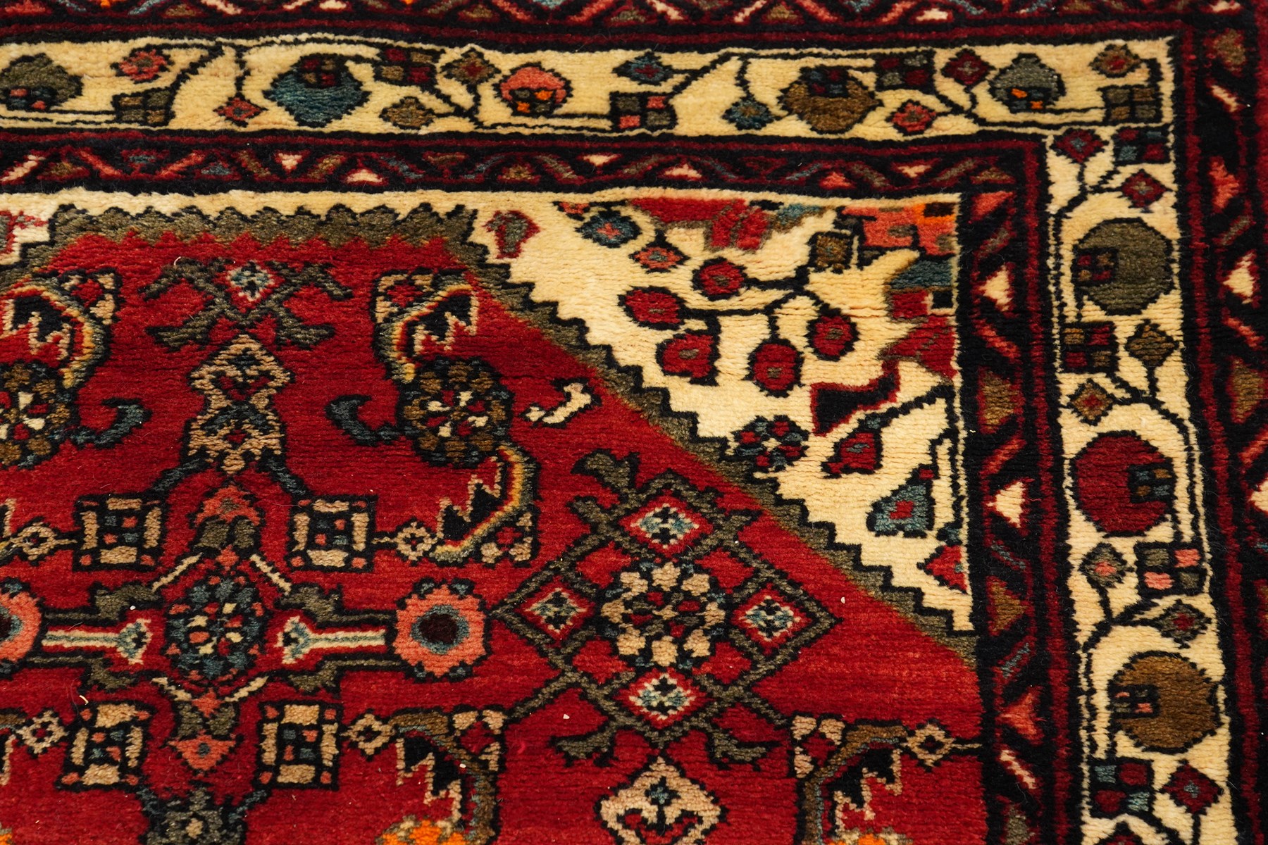 Large Persian Qashqai runner rug, the red ground decorated with navy and ivory lozenge medallions interspersed with stylised floral and geometric motifs, enclosed by an ivory flowerhead border and patterned guard stripes