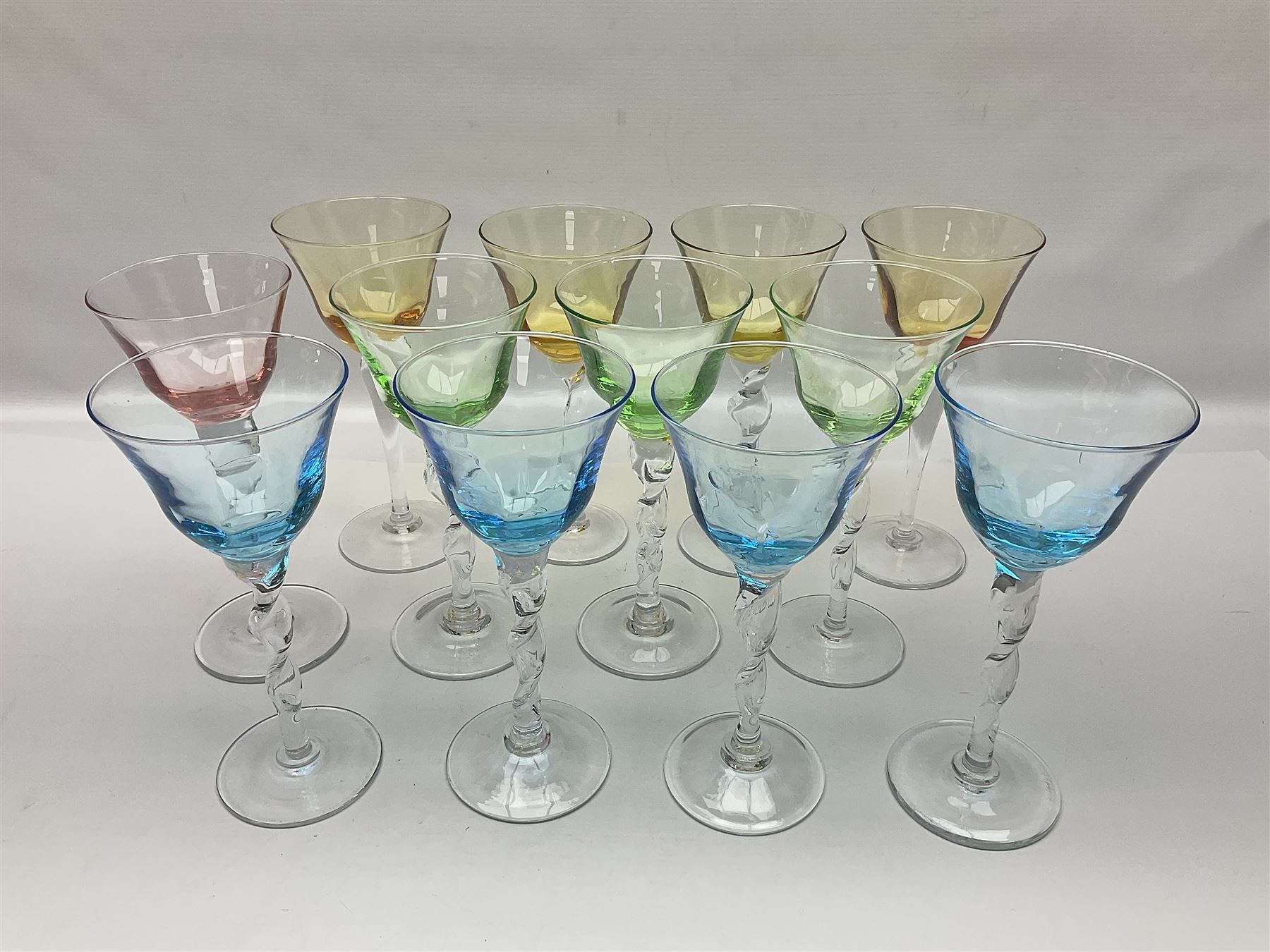 Ten coloured Adriana wine glasses by Abigails, to include blue, green, pink and yellow examples, each with part faceted bowl and twist stems, together with two similar orange examples with pulled stems, H24cm