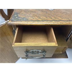 Early 20th century oak smokers cabinet, with brass shield shaped mounts, opening to reveal a compartmentalised interior with three drawers, pipe rack and tobacco jar, together with a small wooden shelf, smokers cabinet H28.5cm