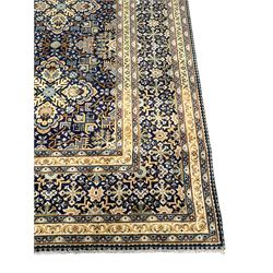 Persian indigo and pale gold ground rug, overall busy geometric design, the field decorated with hooked Hac and palmette medallions surrounded by densely patterned zig-zags and stylised foliate motifs, the border decorated with smaller Hac motifs, within multiple guard stripes 